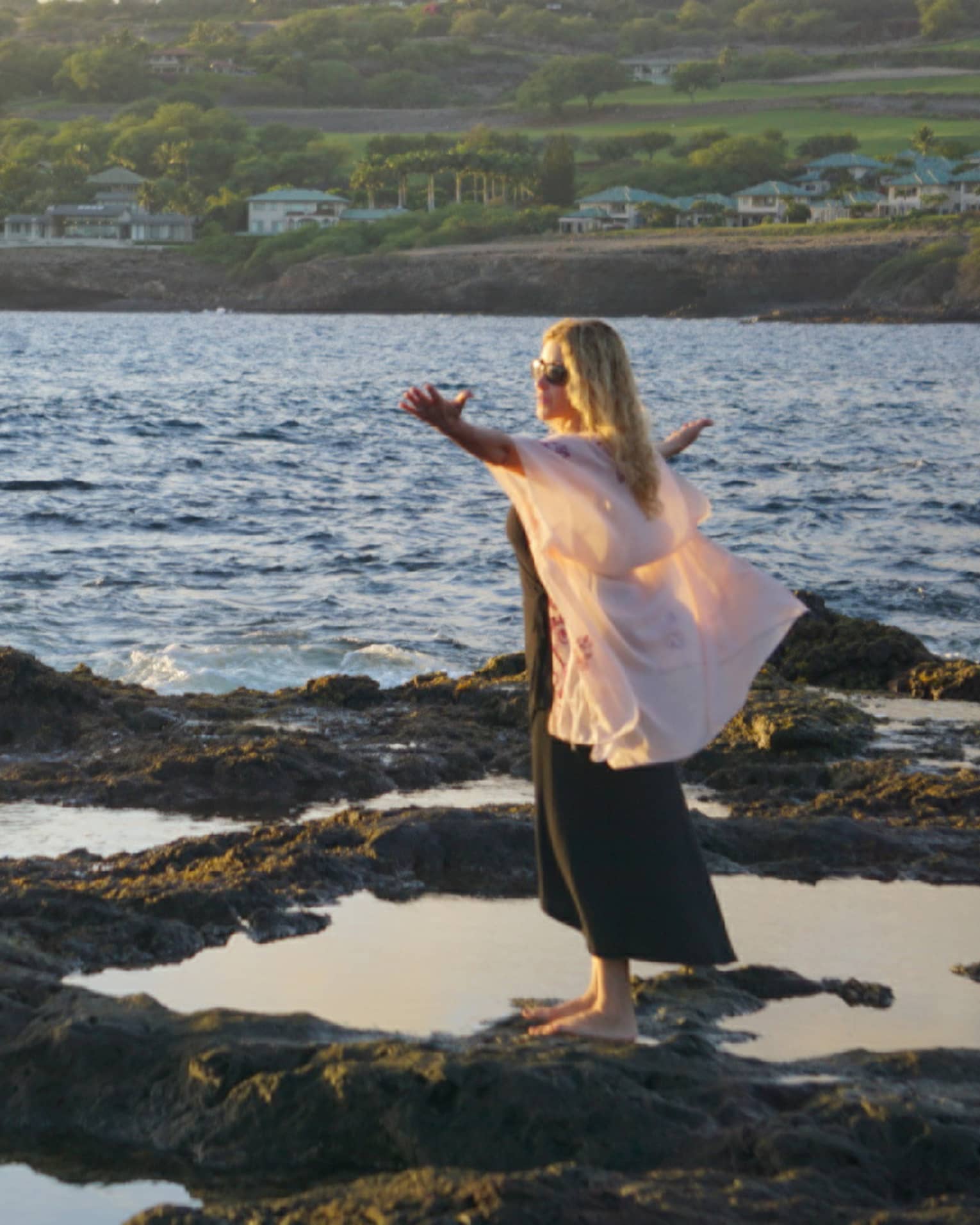 A woman meditates at edge of ocean on lava rock
