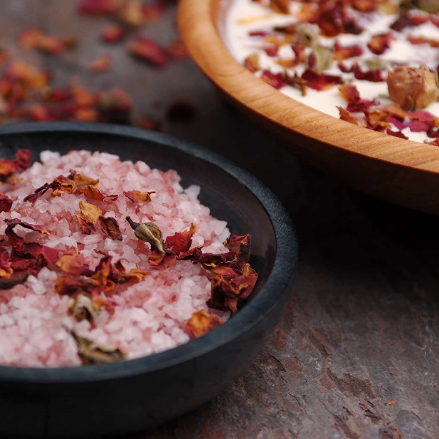 Pink crystals or salt and red flowers in a black bowl.