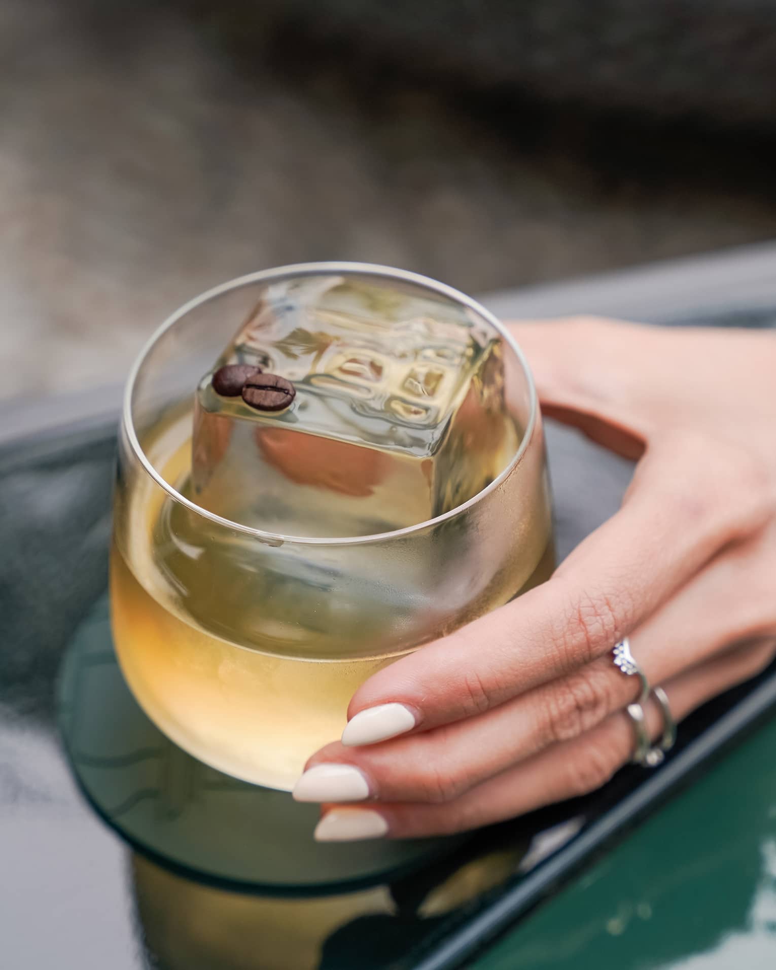 An outstretched hand holds a tan-hued cocktail in a rounded rocks glass