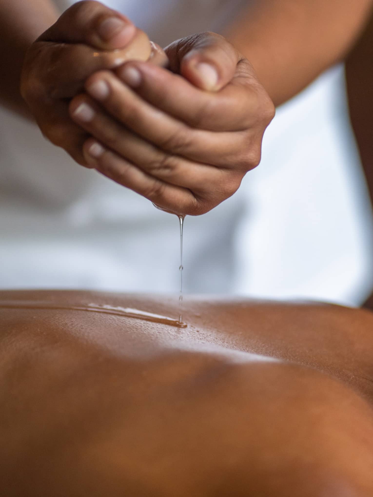 Delicate hands apply oil to a guest's back during a spa treatment