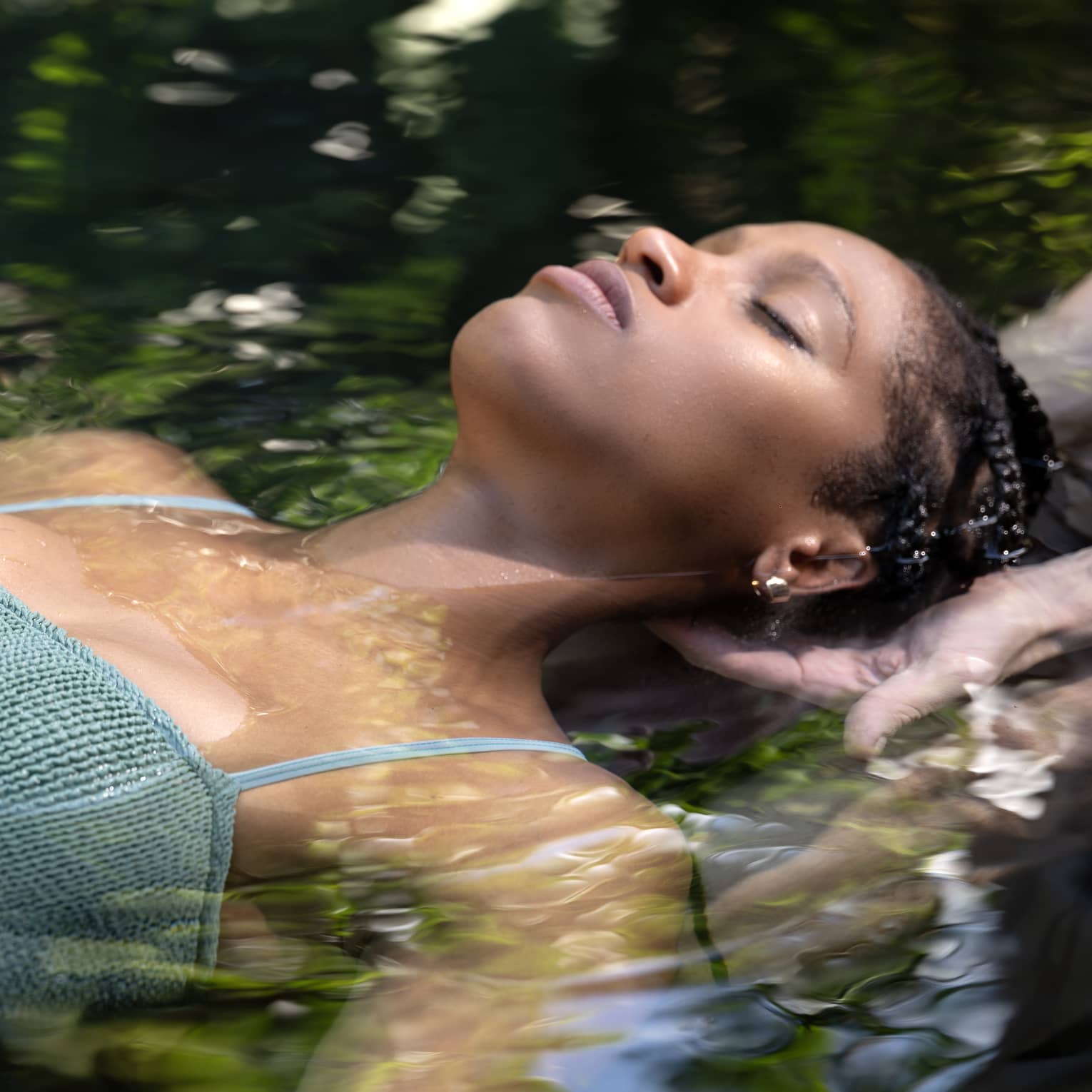 A woman floats in water as two hands lightly hold her head