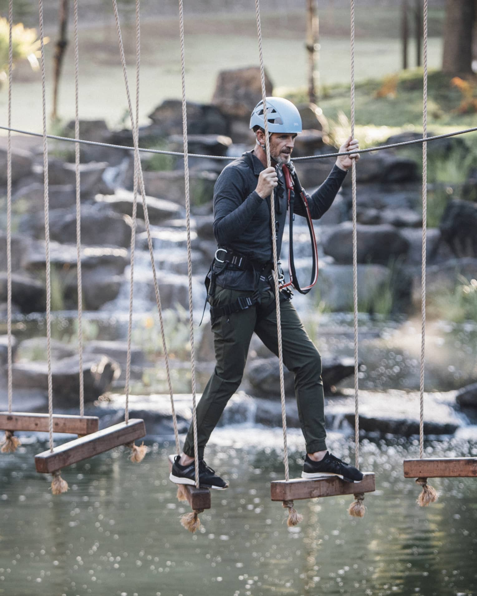 A man walks across hanging wooden blocks at ropes course