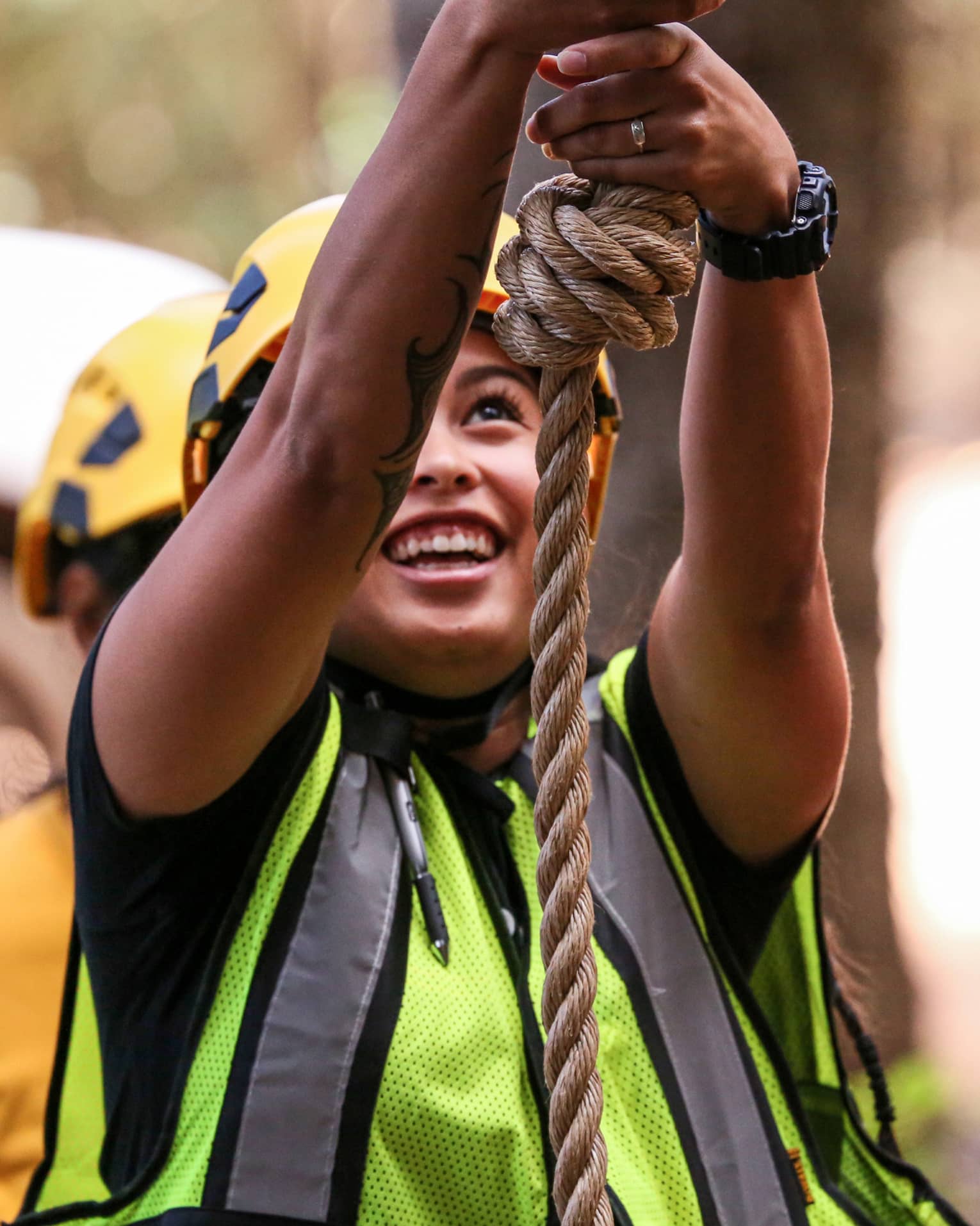 A woman in a helmet and safety vest smiles as she holds on to a rope