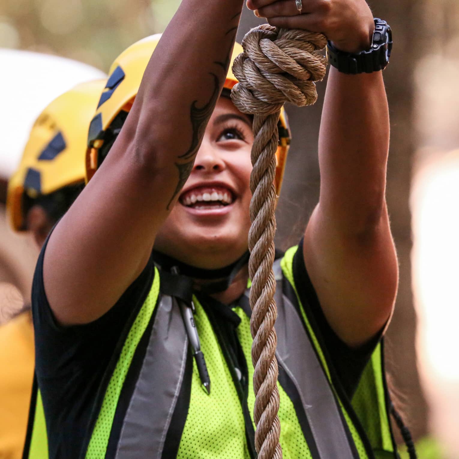 A woman in a helmet and safety vest smiles as she holds on to a rope
