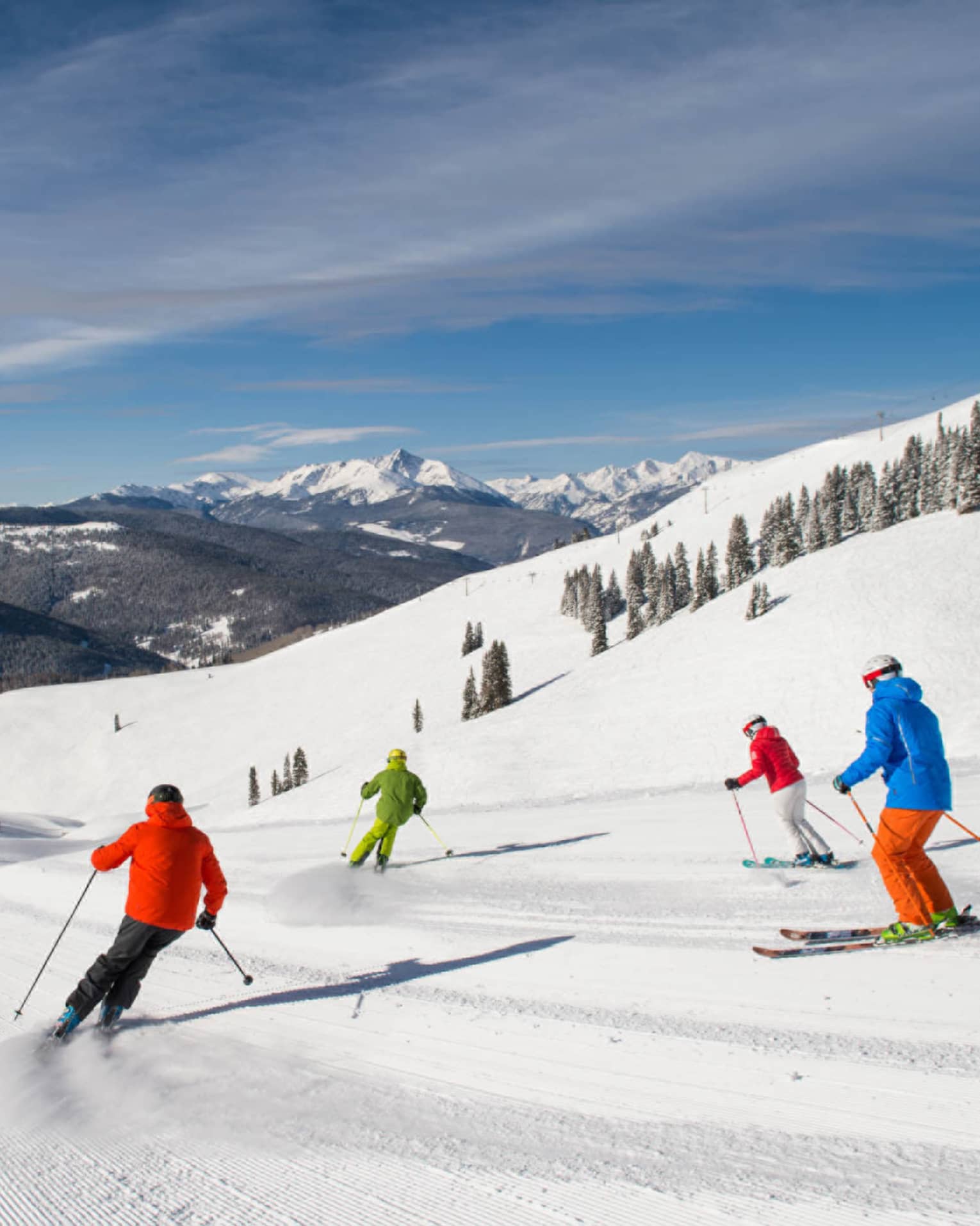 Four skiers in brightly coloured coats ski down mountain covered in snow