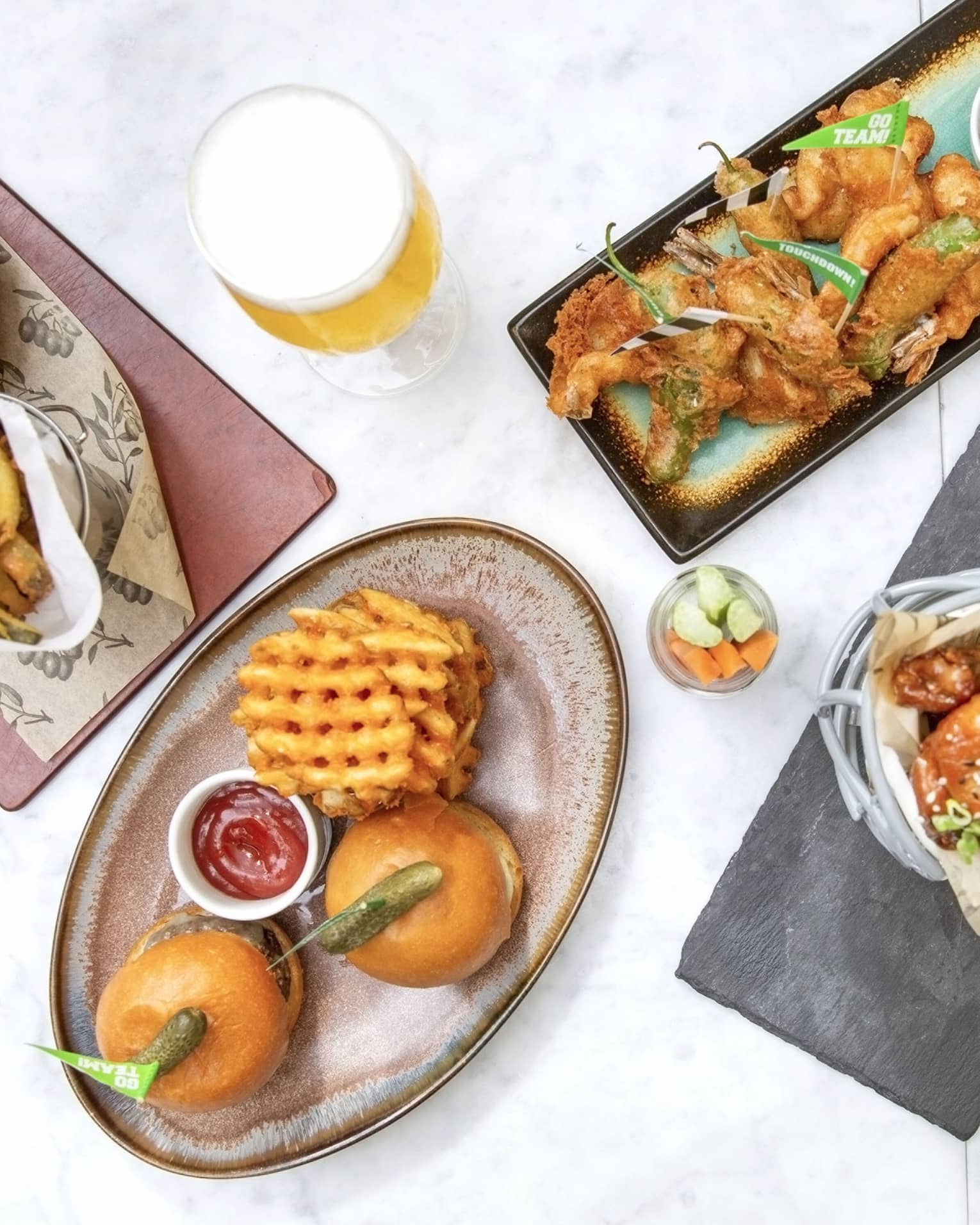 Various food including, chicken wings, hamburgers and fries on rectangular and oval plates.
