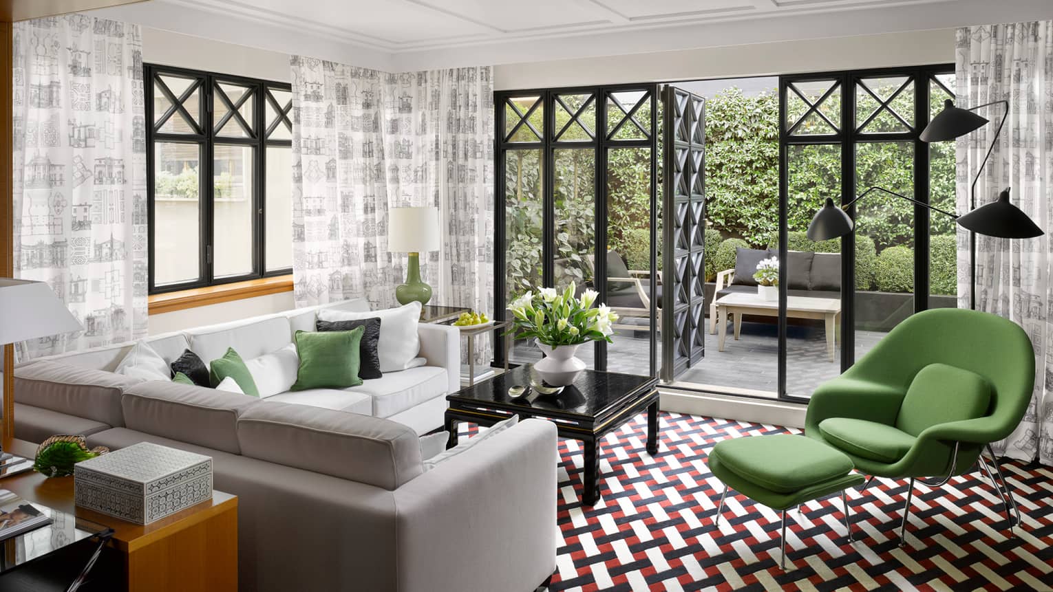 Fashion Suite grey, white sofas, green armchair on retro-style red-and-black tile floor, open balcony doors