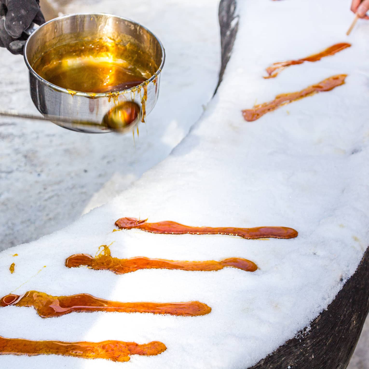 Person ladles hot maple syrup in rows on top of snow-covered surface