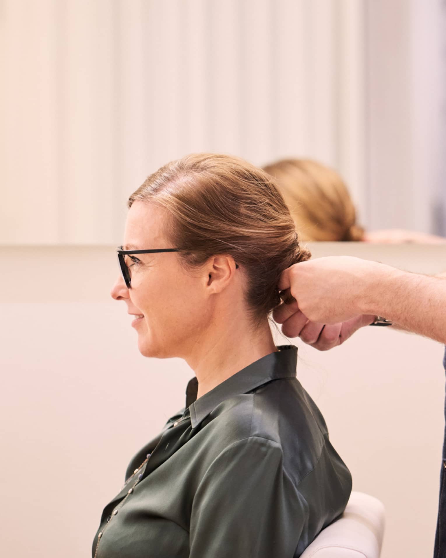 Woman sits in salon chair as hair stylist with long beard holds her hair