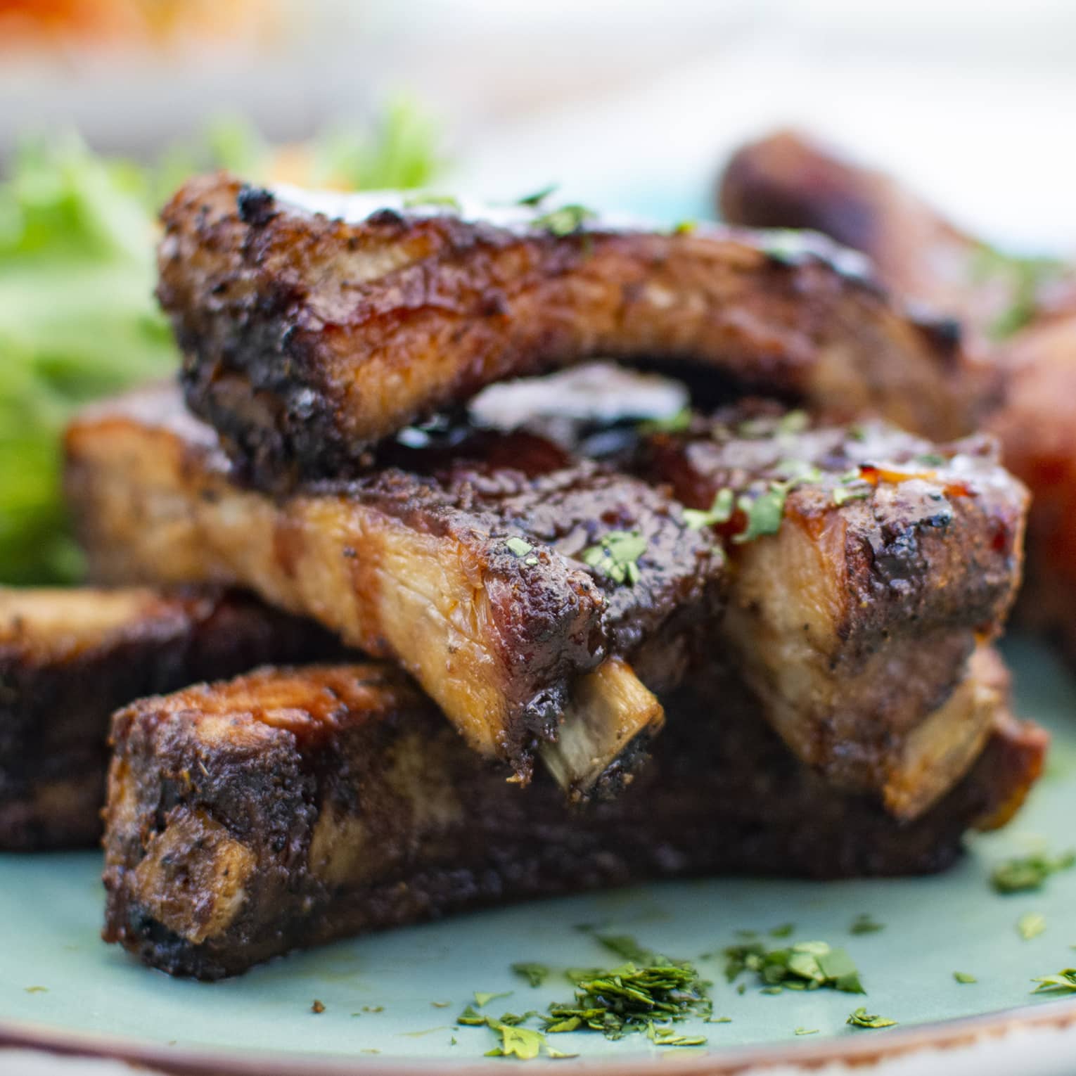 Close-up of a plate of sauce-crusted barbecue ribs and chicken drumsticks sprinkled with chopped fresh herbs.