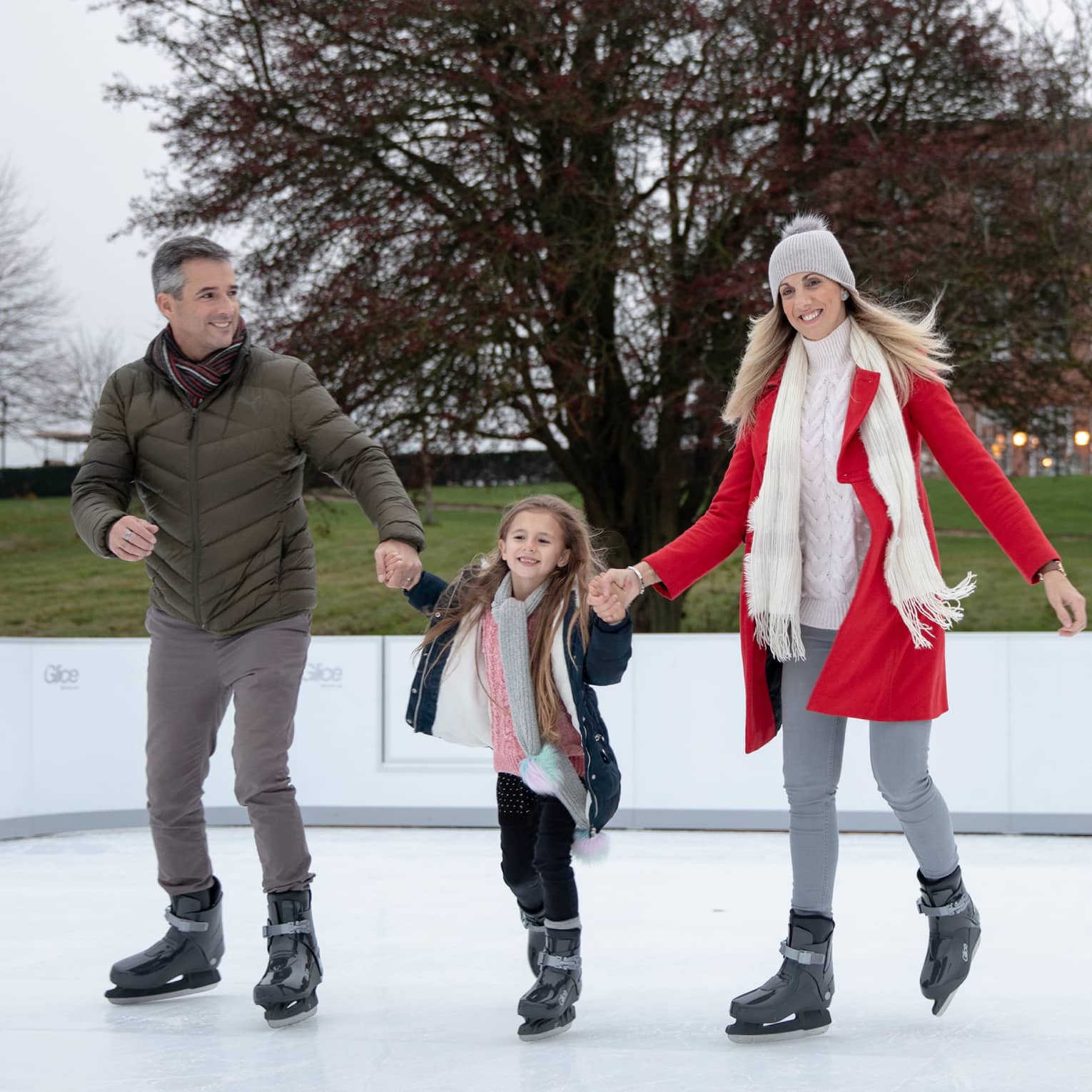 Man and woman holding hands of young girl while ice skating on outdoor rink