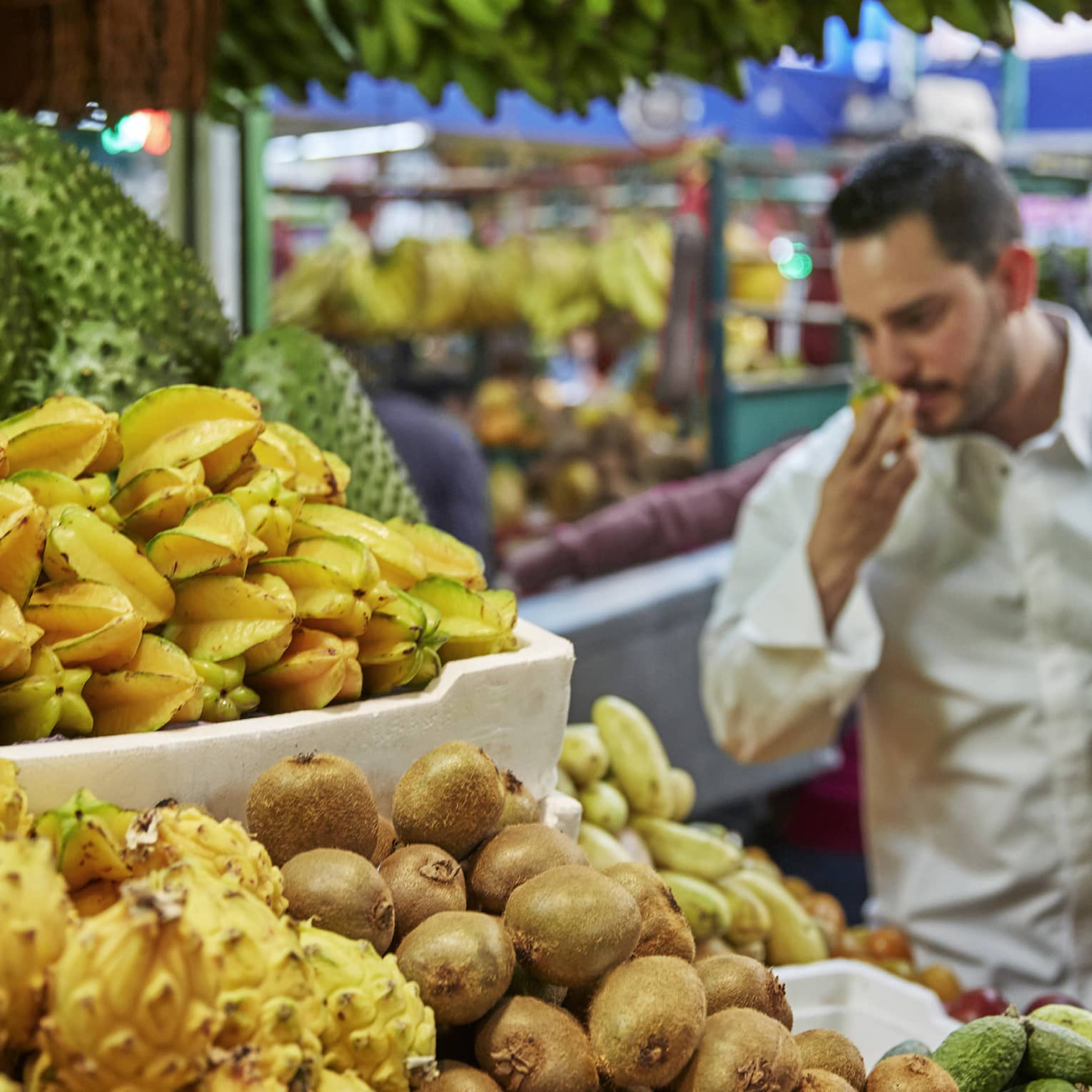 Chef smells tropical fruit at stand in market 