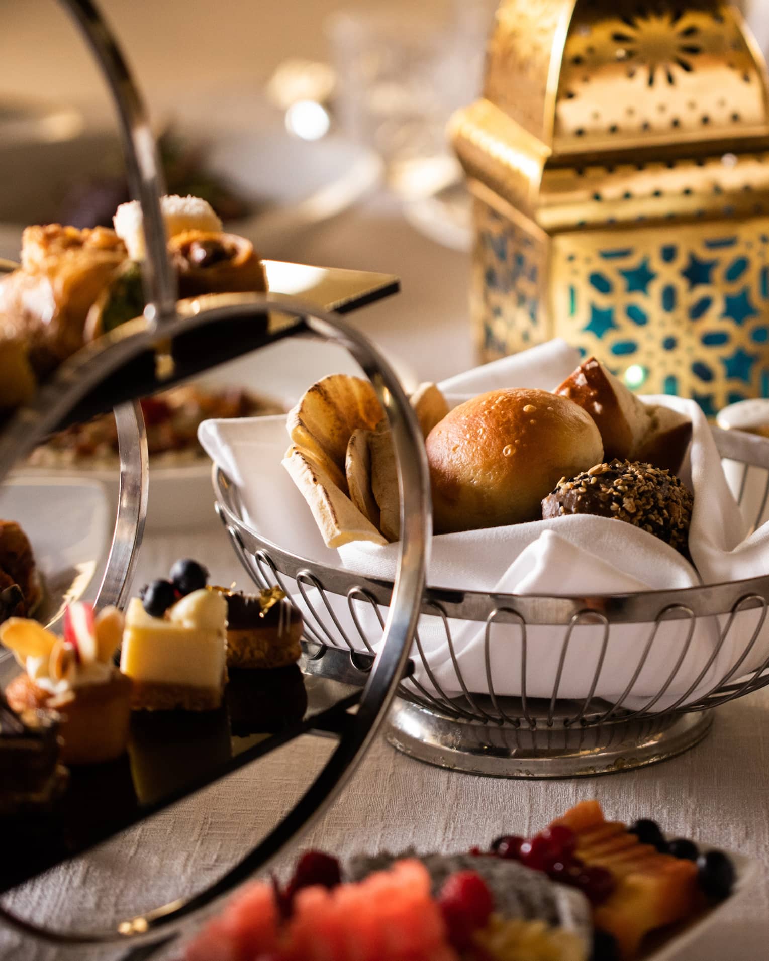 A gold lantern, silver bread basket and various platters filled with miniature desserts sit on a white-linen table