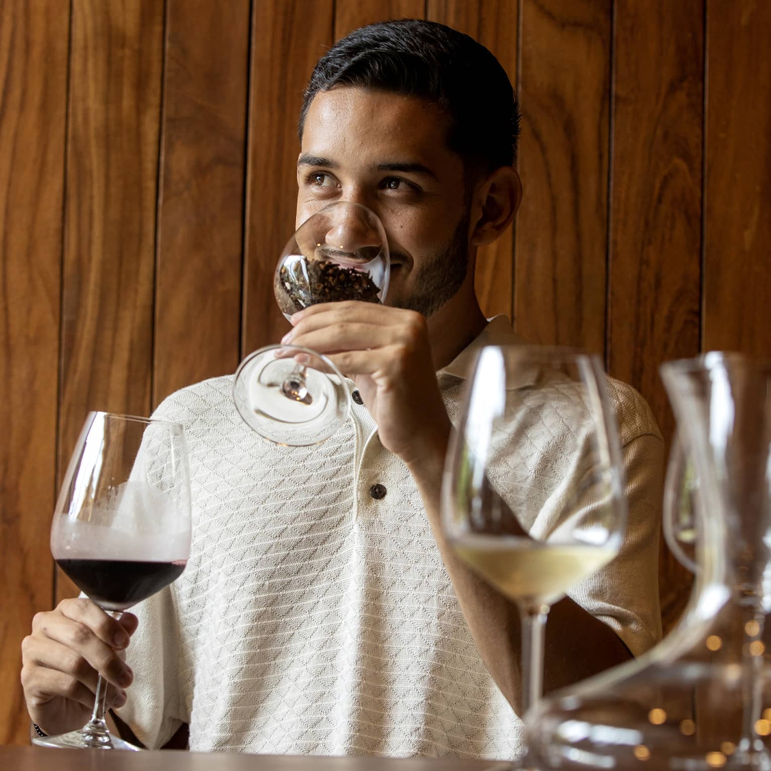 At a wine tasting, a guest smells coffee beans in a glass before tasting the glass of dark red wine held in his other hand. 