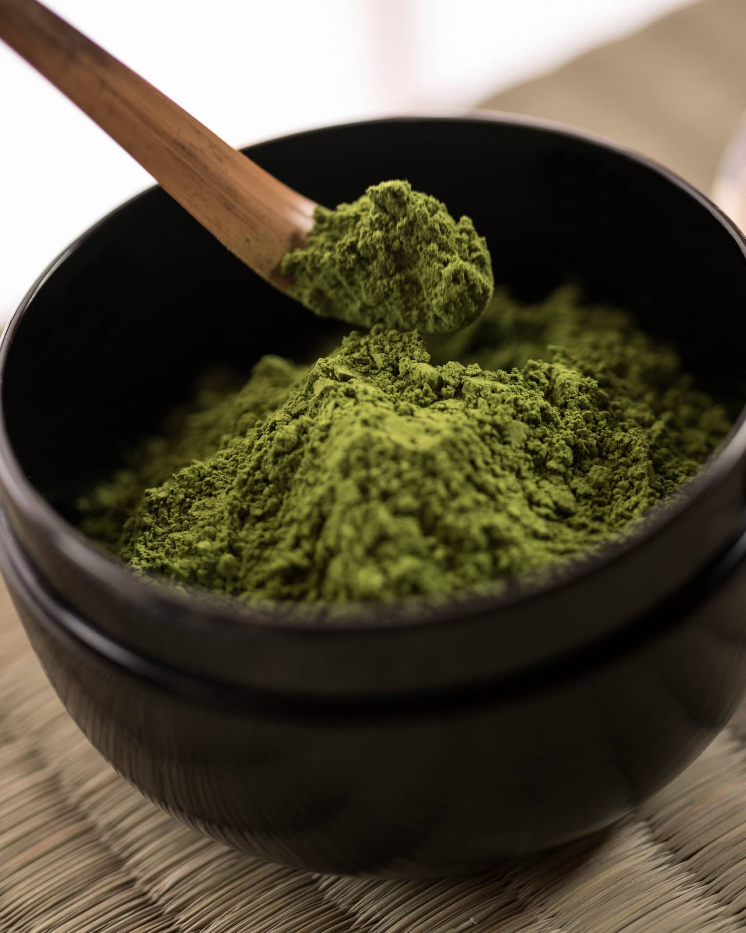 Close-up of green matcha tea powder in small black bowl, wood spoon