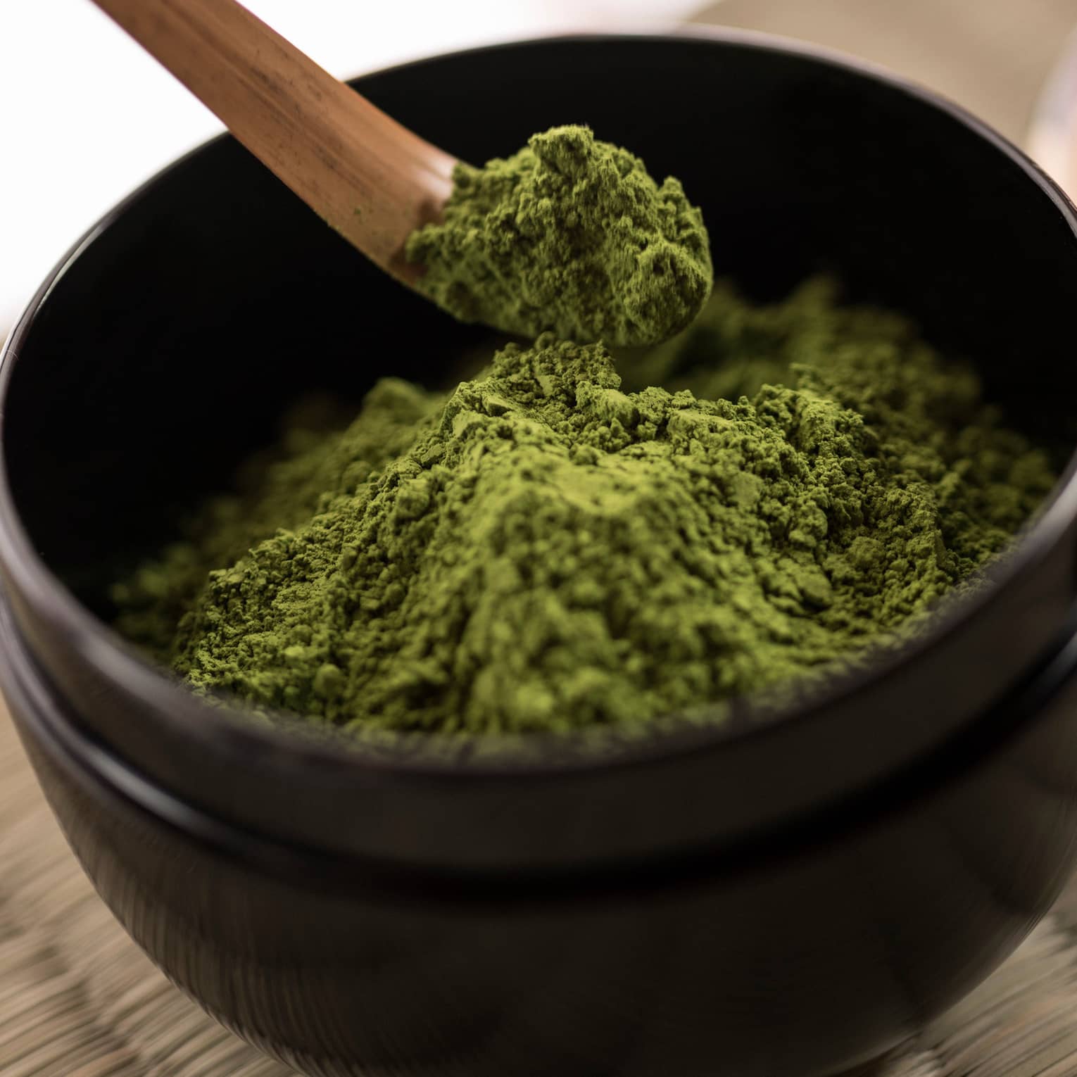 Close-up of green matcha tea powder in small black bowl, wood spoon