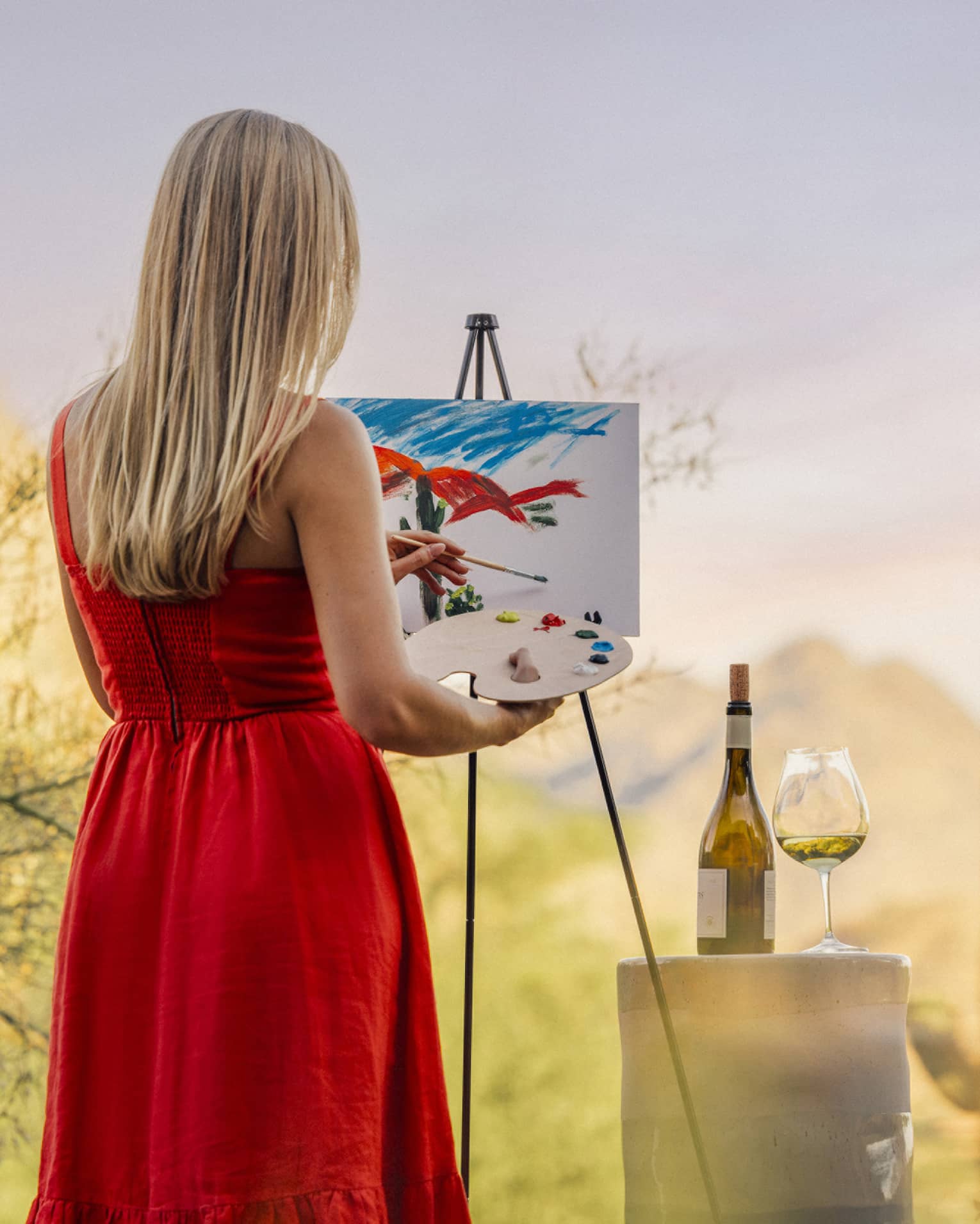 Person wearing a red dress and painting with a wine glass beside them.