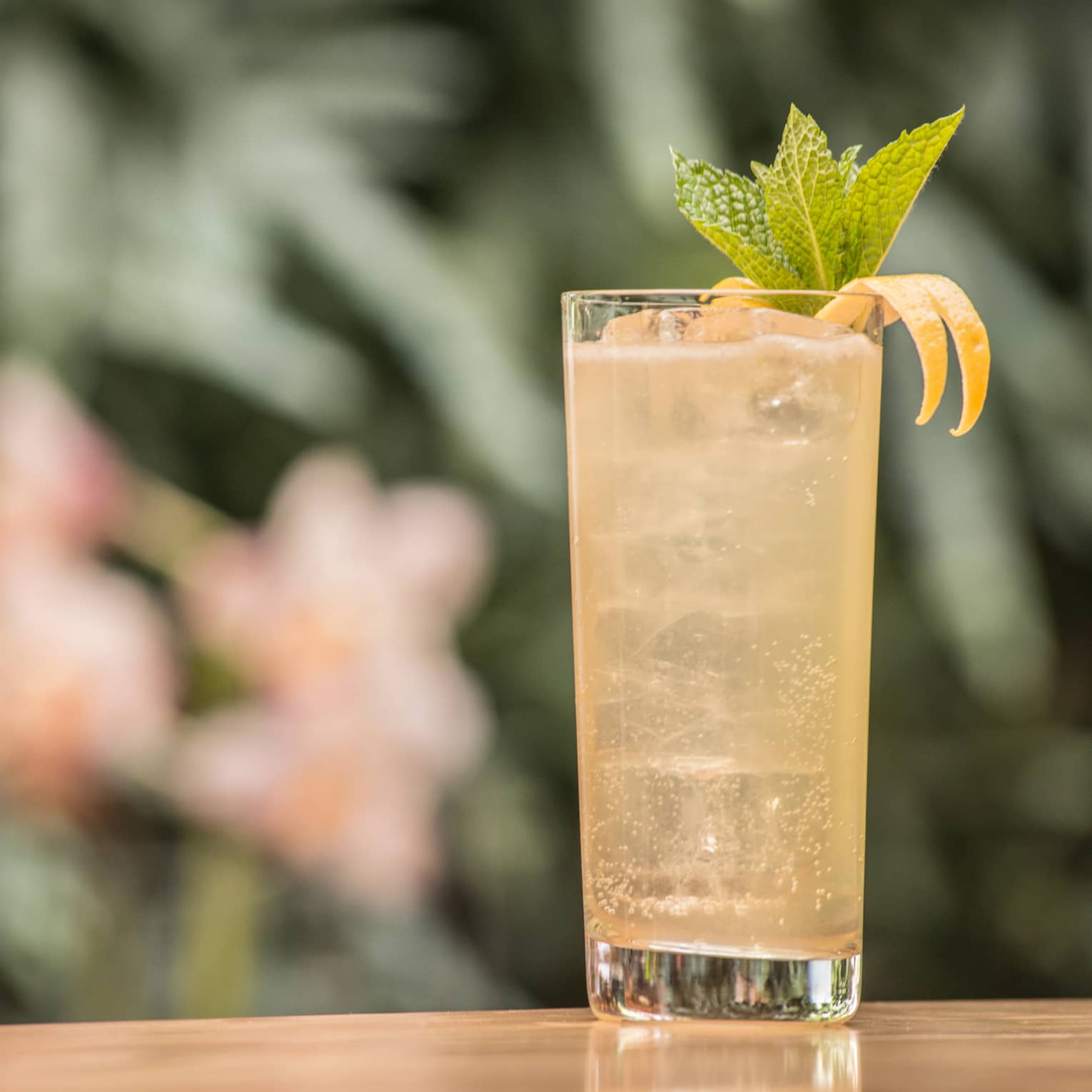 A tall glass filled with a yellow cocktail and several mint leaves. 