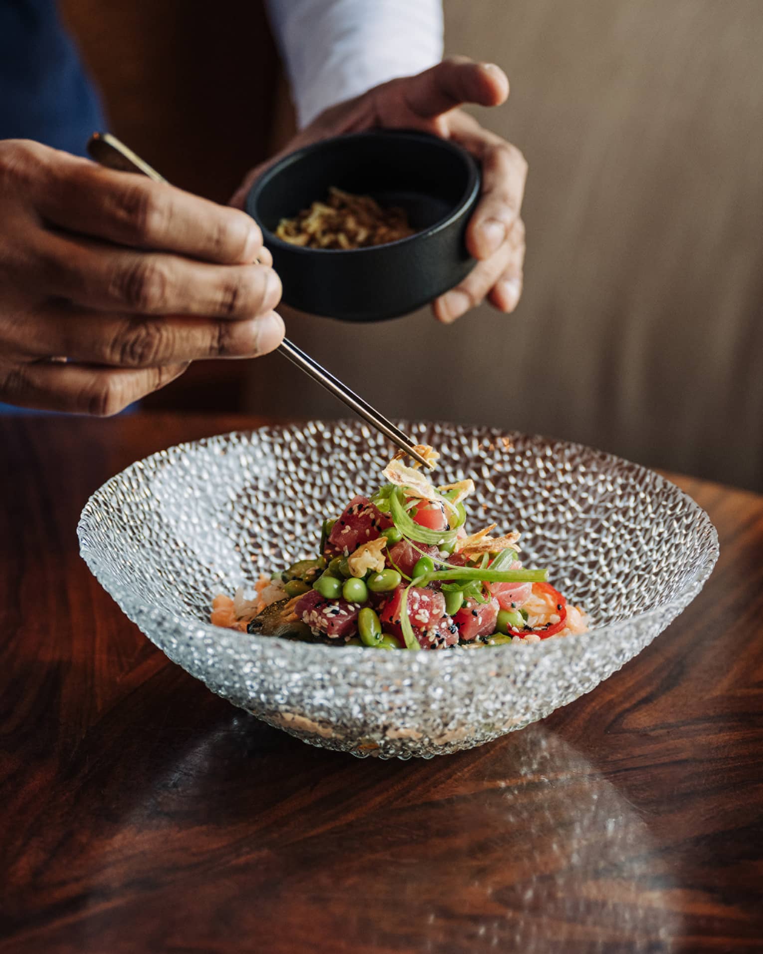 Waiter uses chopsticks to place item on top of salad in a clear glass bowl