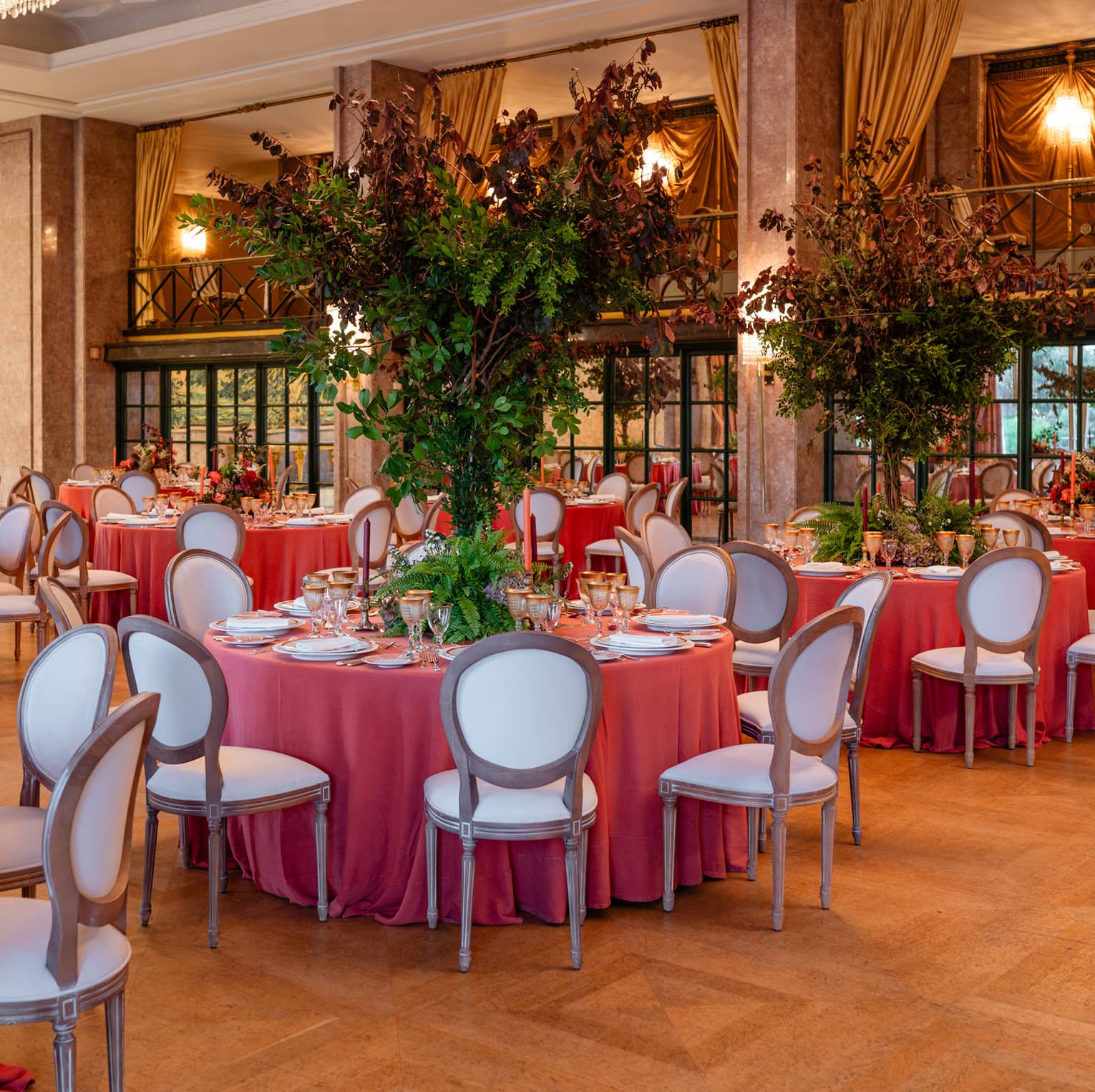 Elegant ballroom set for a formal event, with table rounds featuring coral-coloured tablecloths and tall floral centrepieces