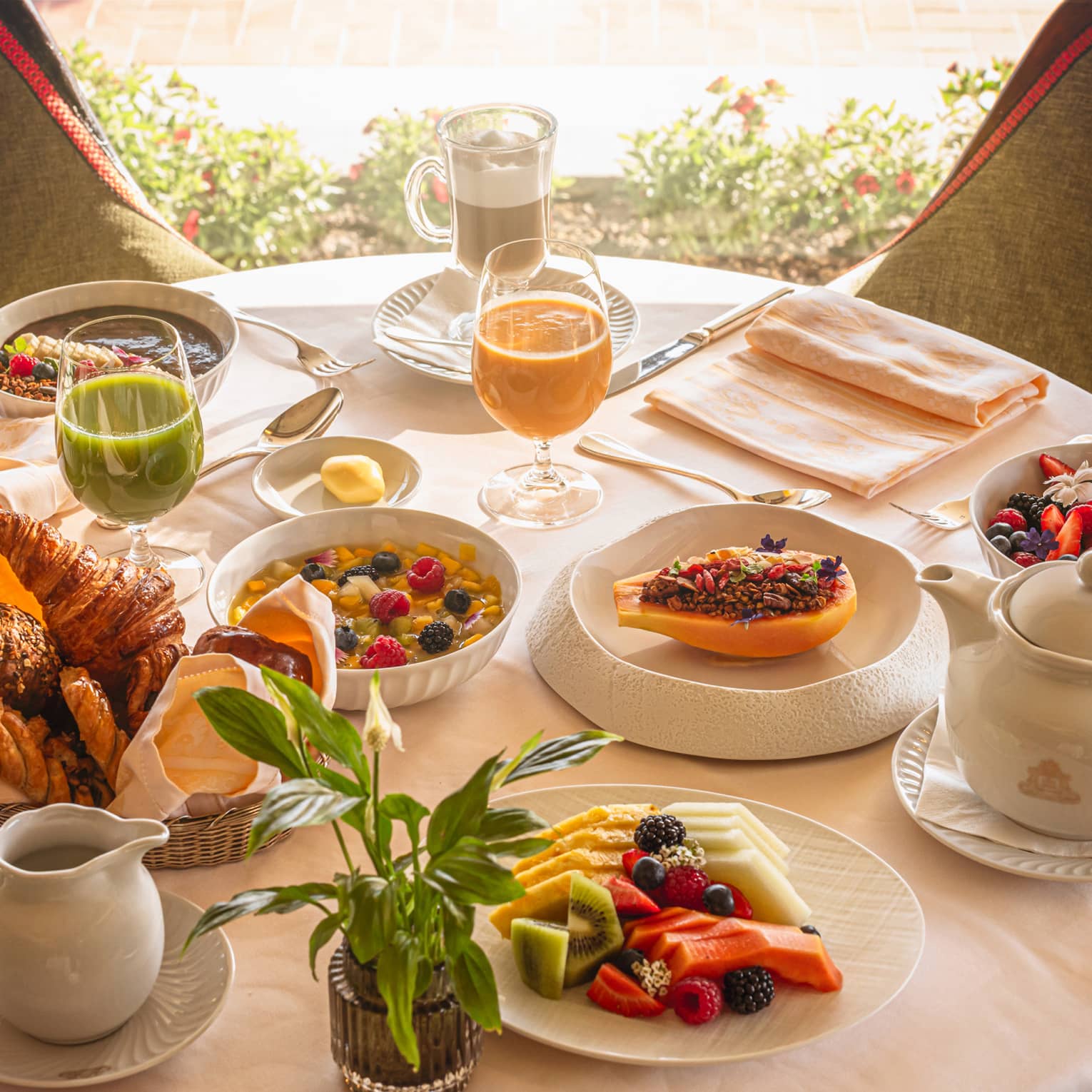 A round table in front of a window, set with an array of brunch dishes and beverages