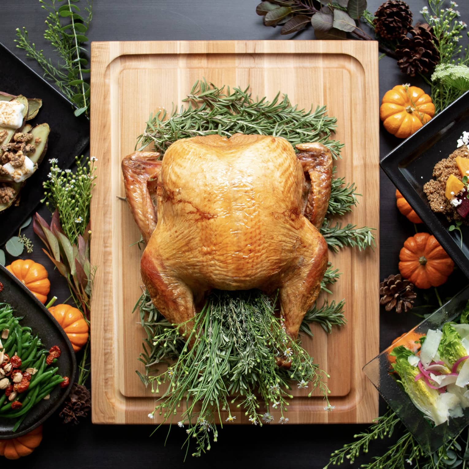 A turkey on a wooden board with other Thanksgiving foods around it.