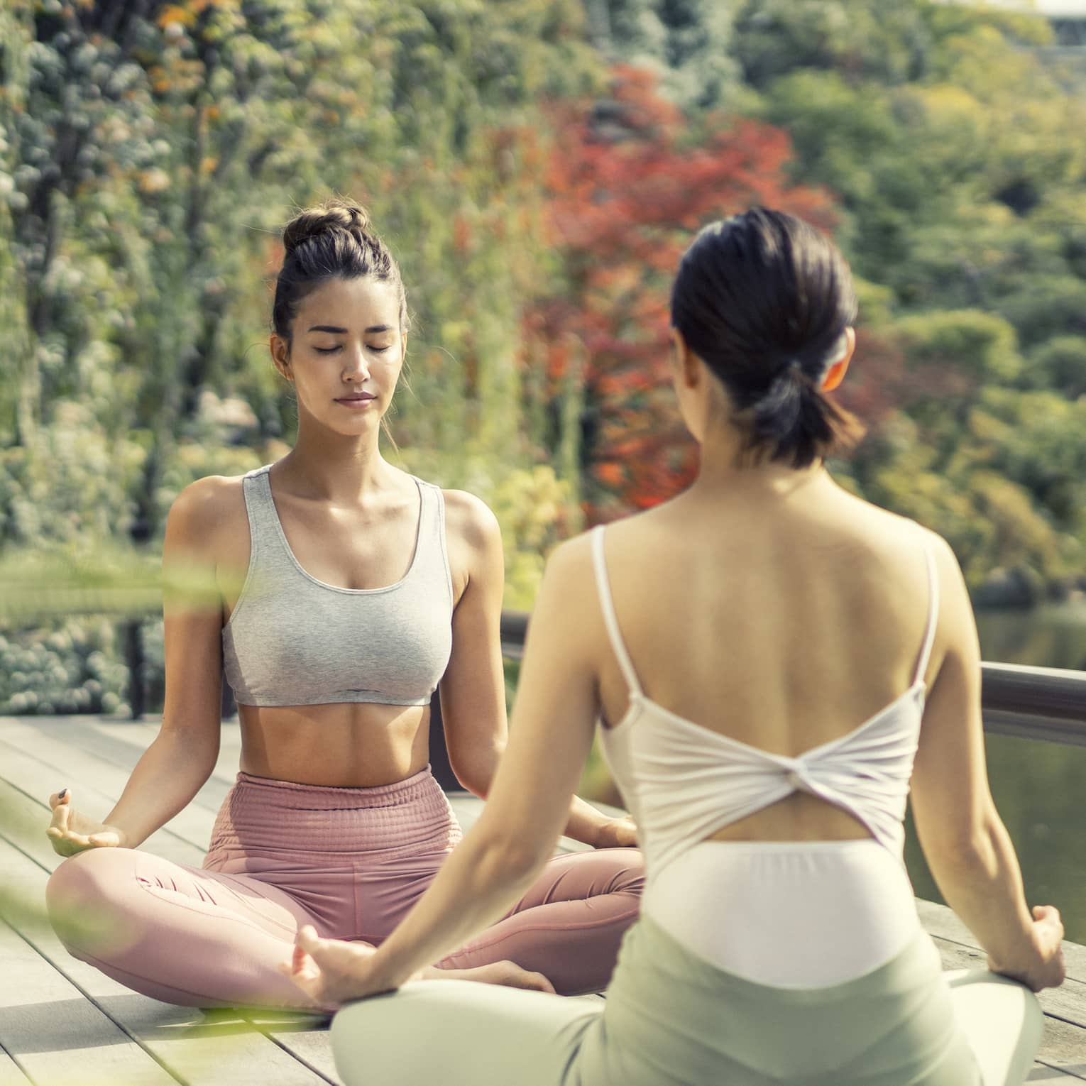 Two women sit cross-legged in a yoga pose in the Shakusui-en pond garden