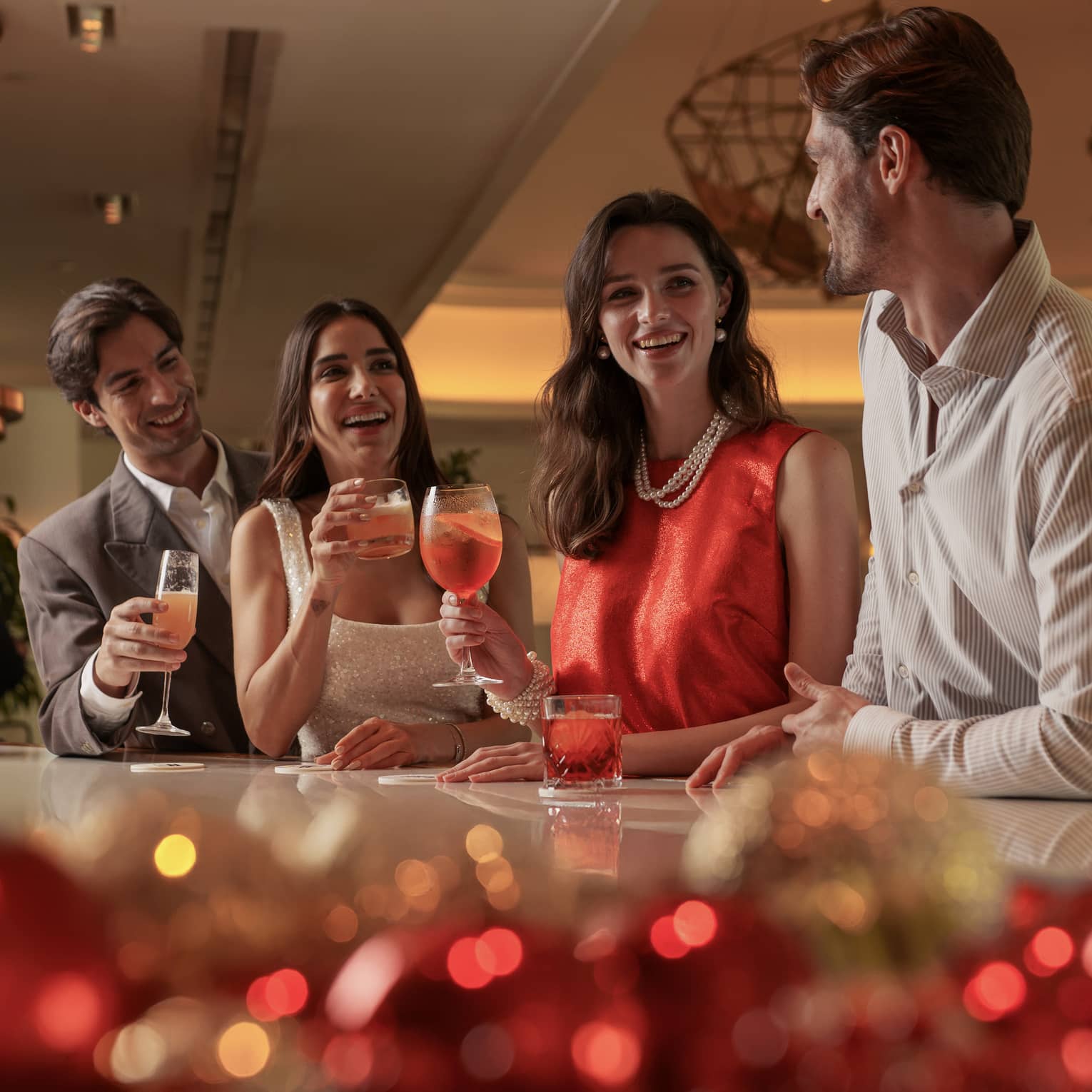 Group of four dressed in casual cocktail attire stand smiling at a white marble bar decorated with red and gold ornaments