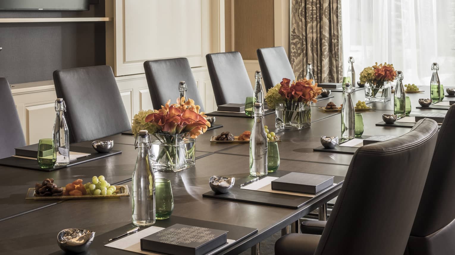 Long boardroom table set with glass bottles of water, flowers in bright meeting room