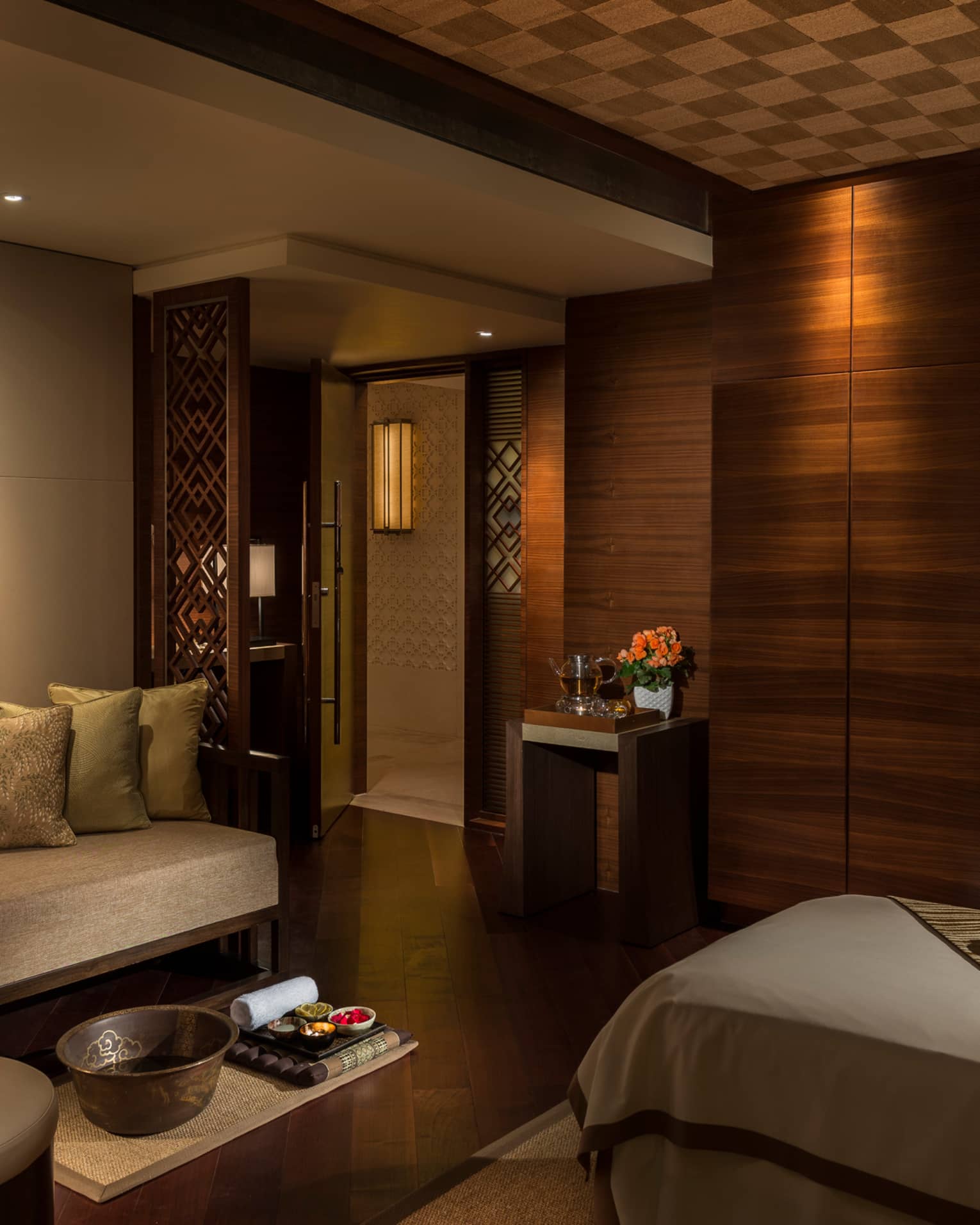 Spa treatment room with carved wood detail walls, bed and table with trays with oils