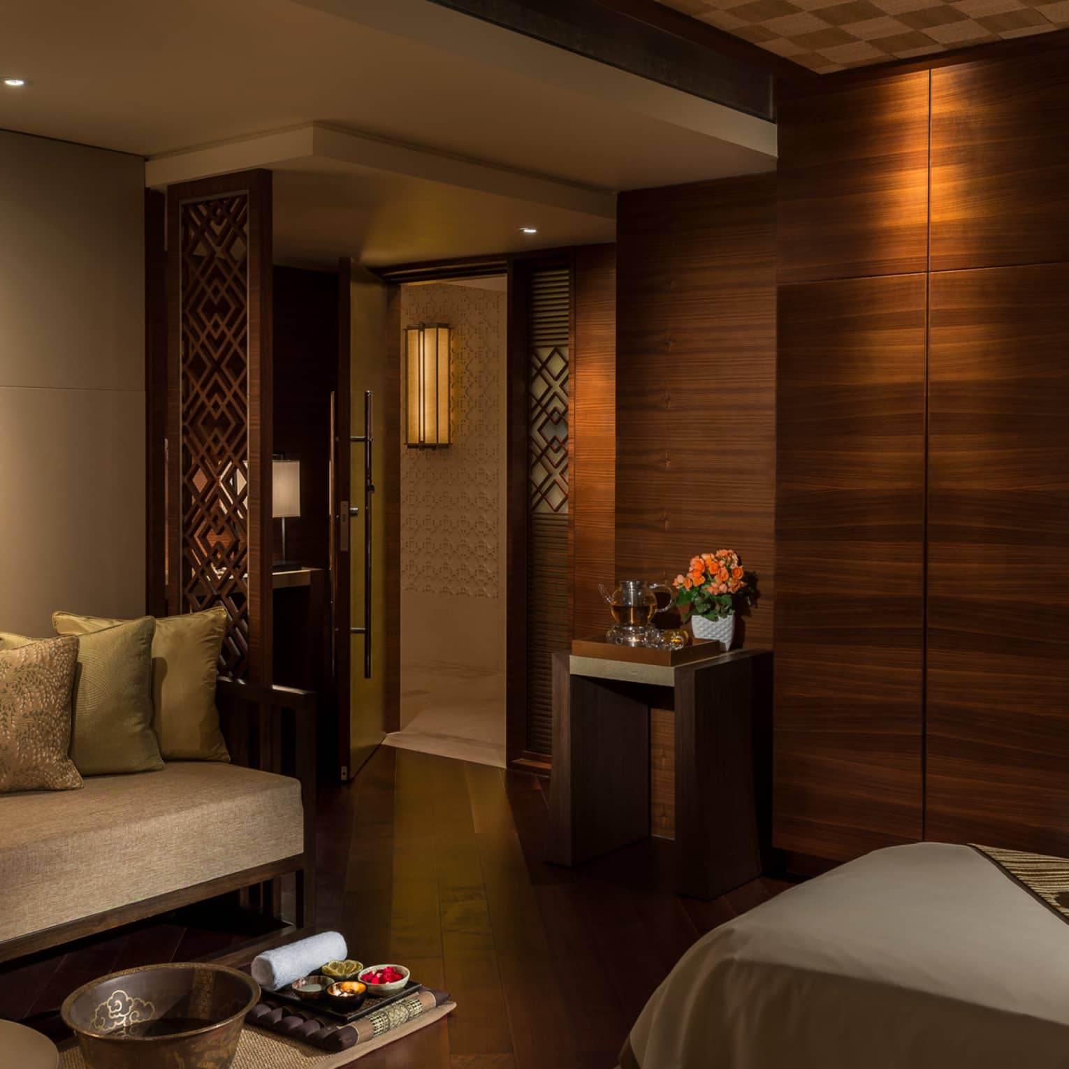 Spa treatment room with carved wood detail walls, bed and table with trays with oils
