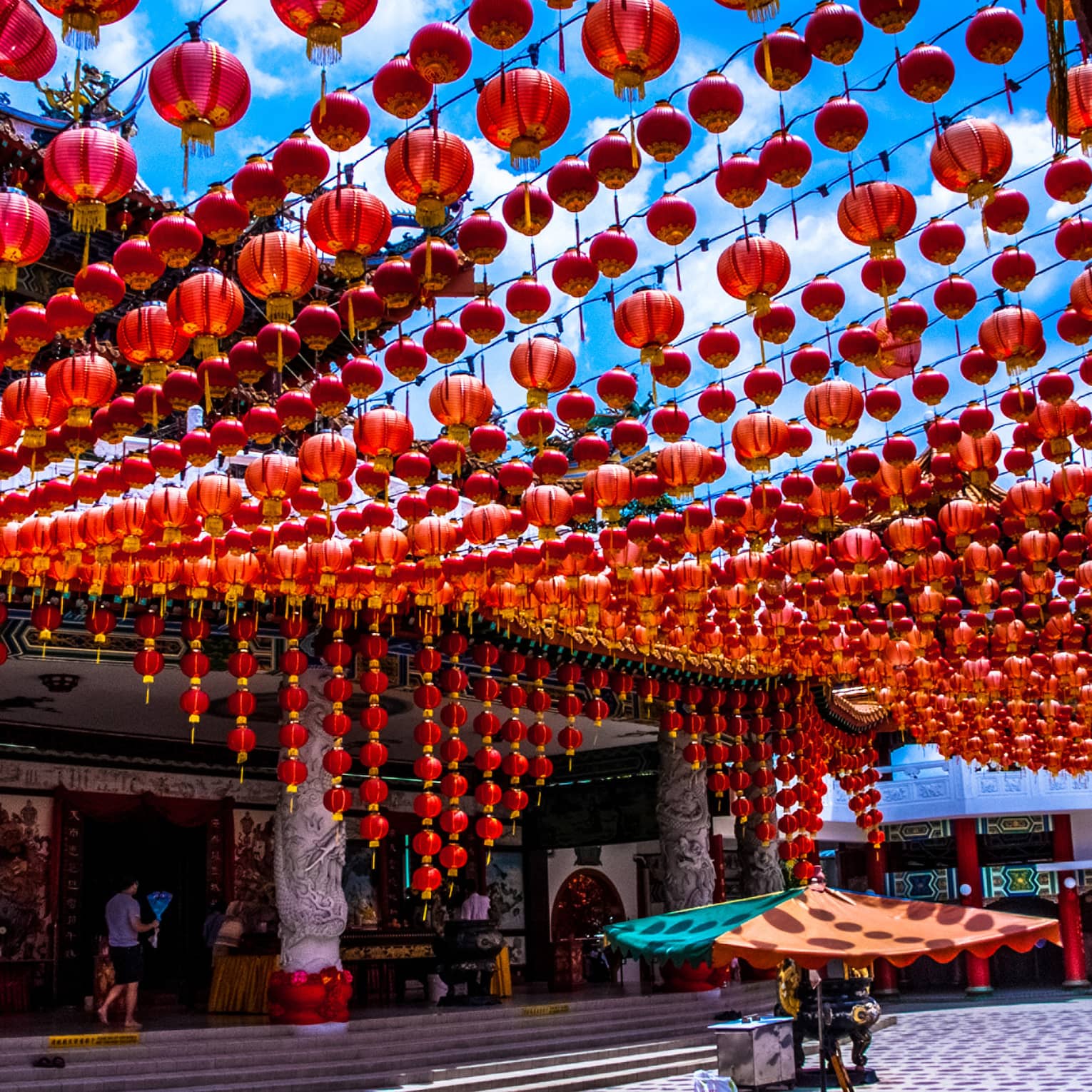 A temple’s entrance features pillars embellished by intricate carvings. Hundreds of crimson red lanterns are strung overhead.