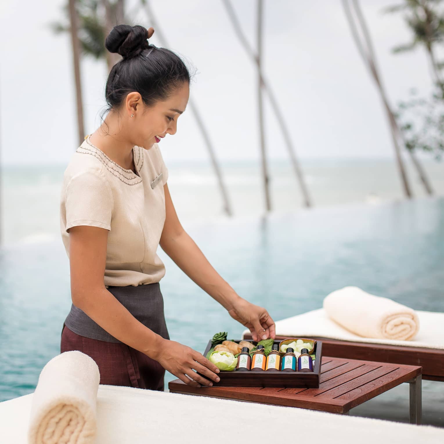 Spa attendant stands in front of swimming pool, holds wood box with bottles, soaps