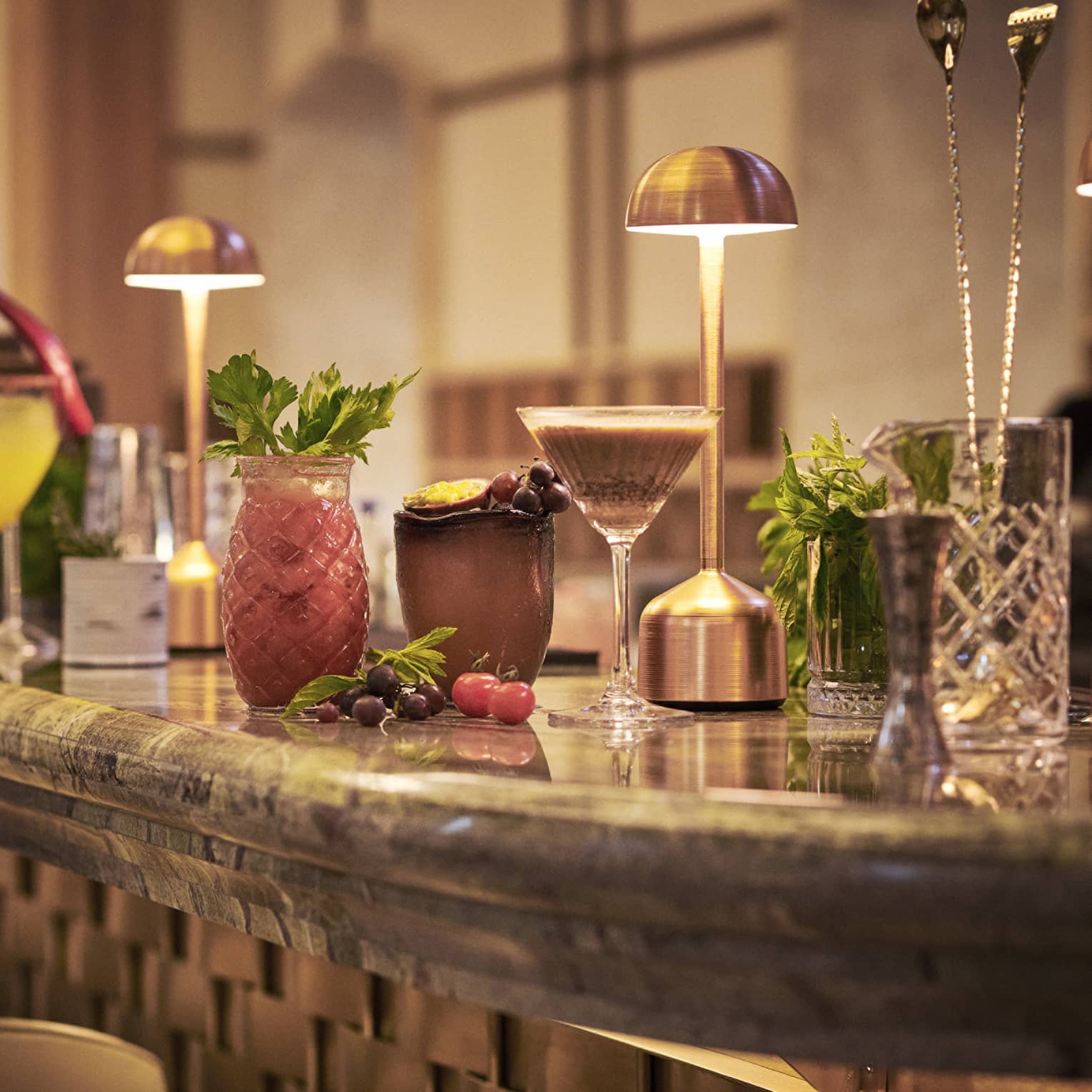 Cocktails in various glassware lined up on bar under copper desk lights