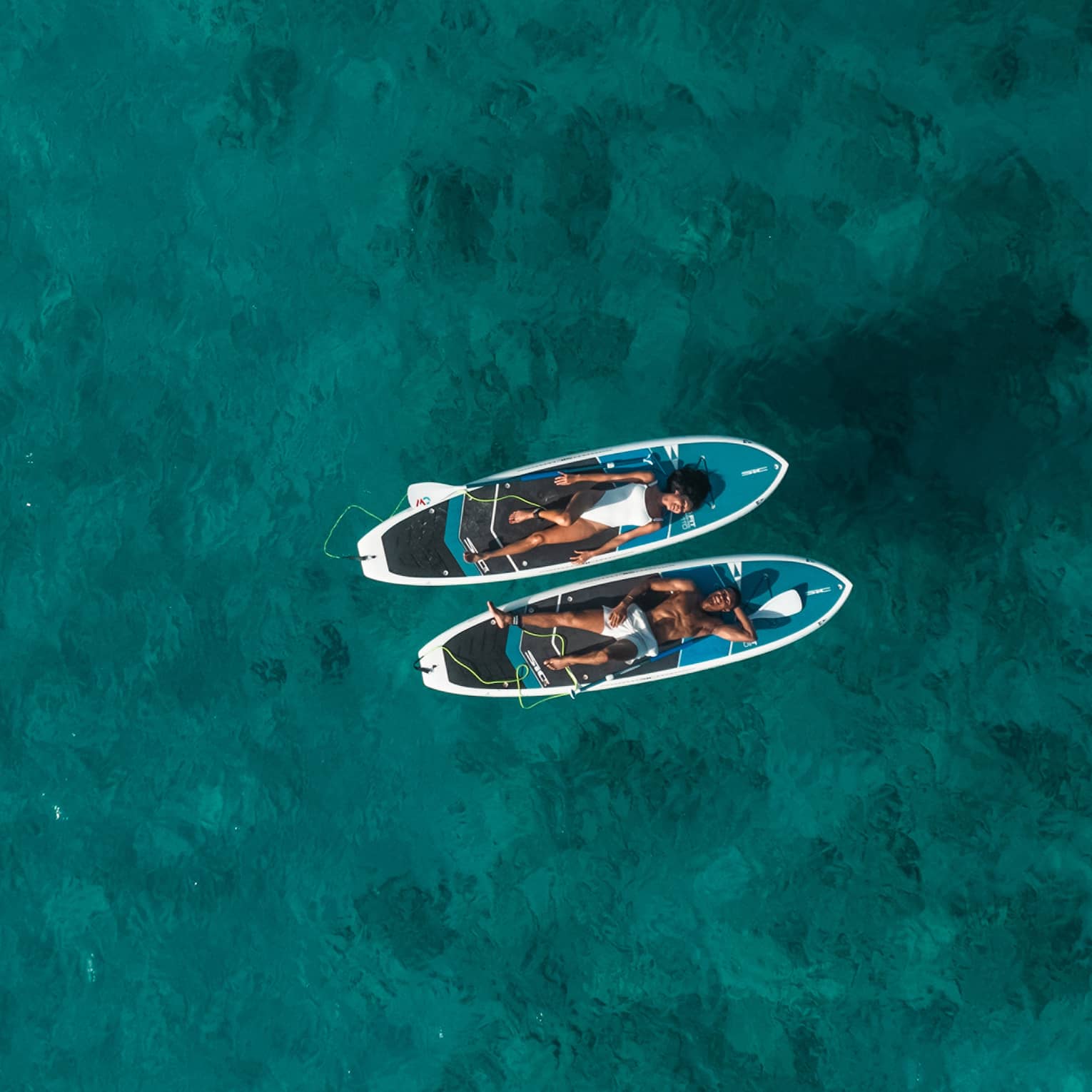 Two people lay on SUP paddleboards on the water