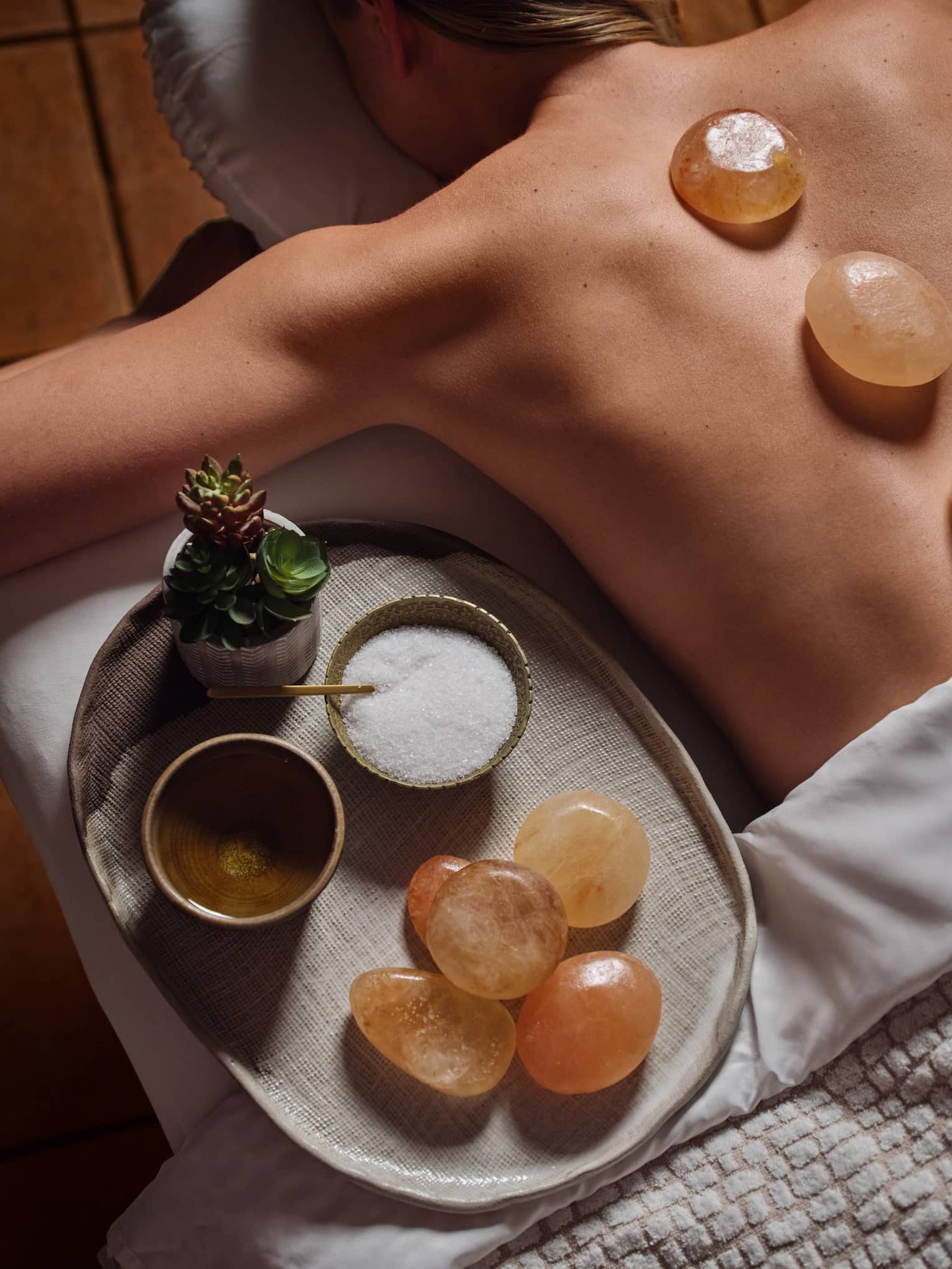 Person laying on a massage table with three stones on their back.