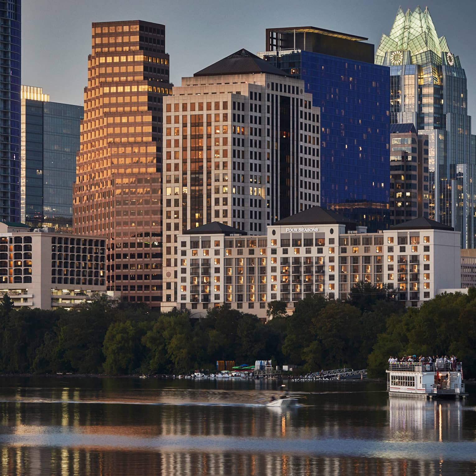 Buildings, trees, small ferry boat on water along Lady Bird Lake Austin waterfront