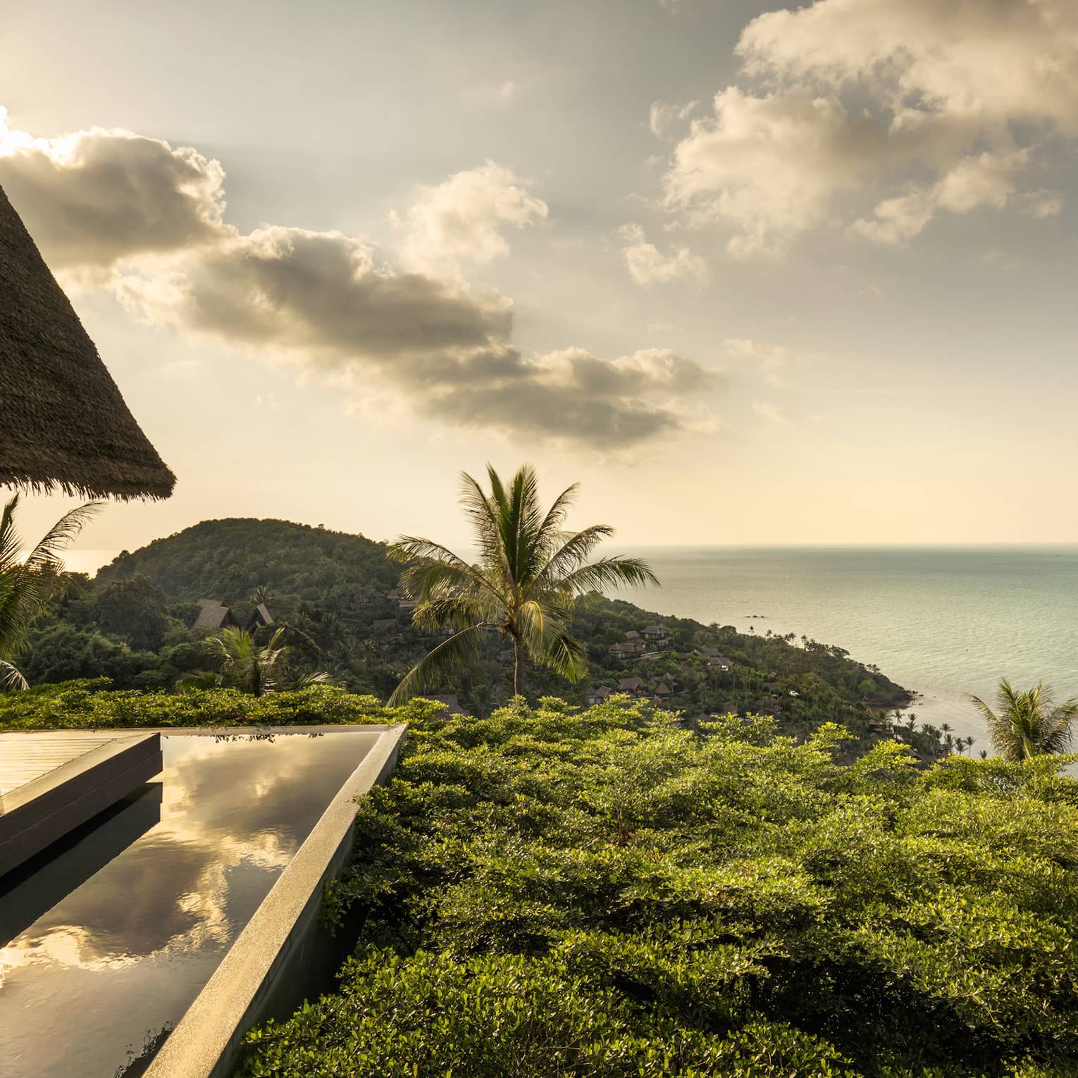 Patio lounge chair, thatched roof and deck overlooking canopy of tropical trees, ocean