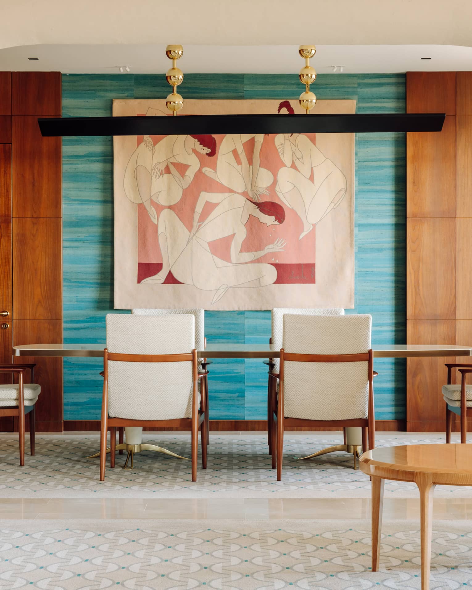 Elegant dining area with a long table, white chairs, colorful wall art and wood-paneled walls framed by an arched entryway.