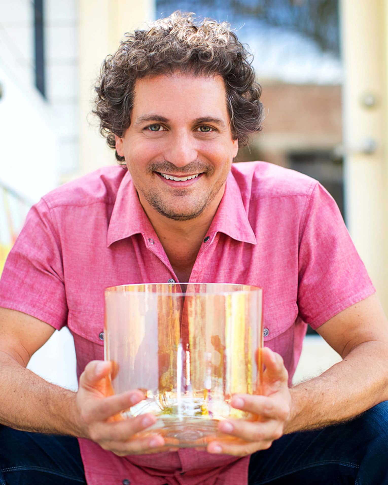 Sound Practitioner David Kennet in pink button-down and jeans, holding a crystal singing bowl