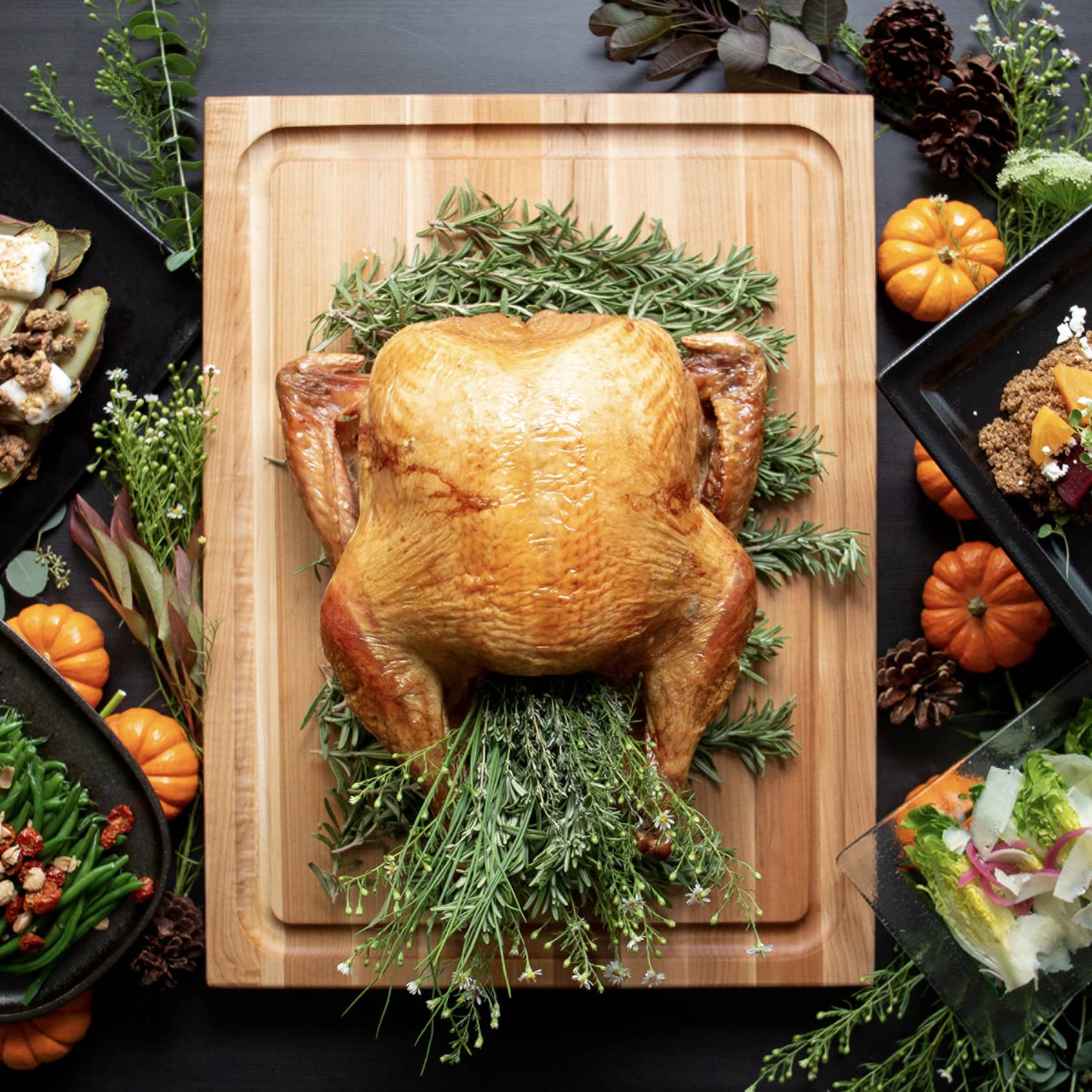 A turkey on a wooden board with other Thanksgiving foods around it.