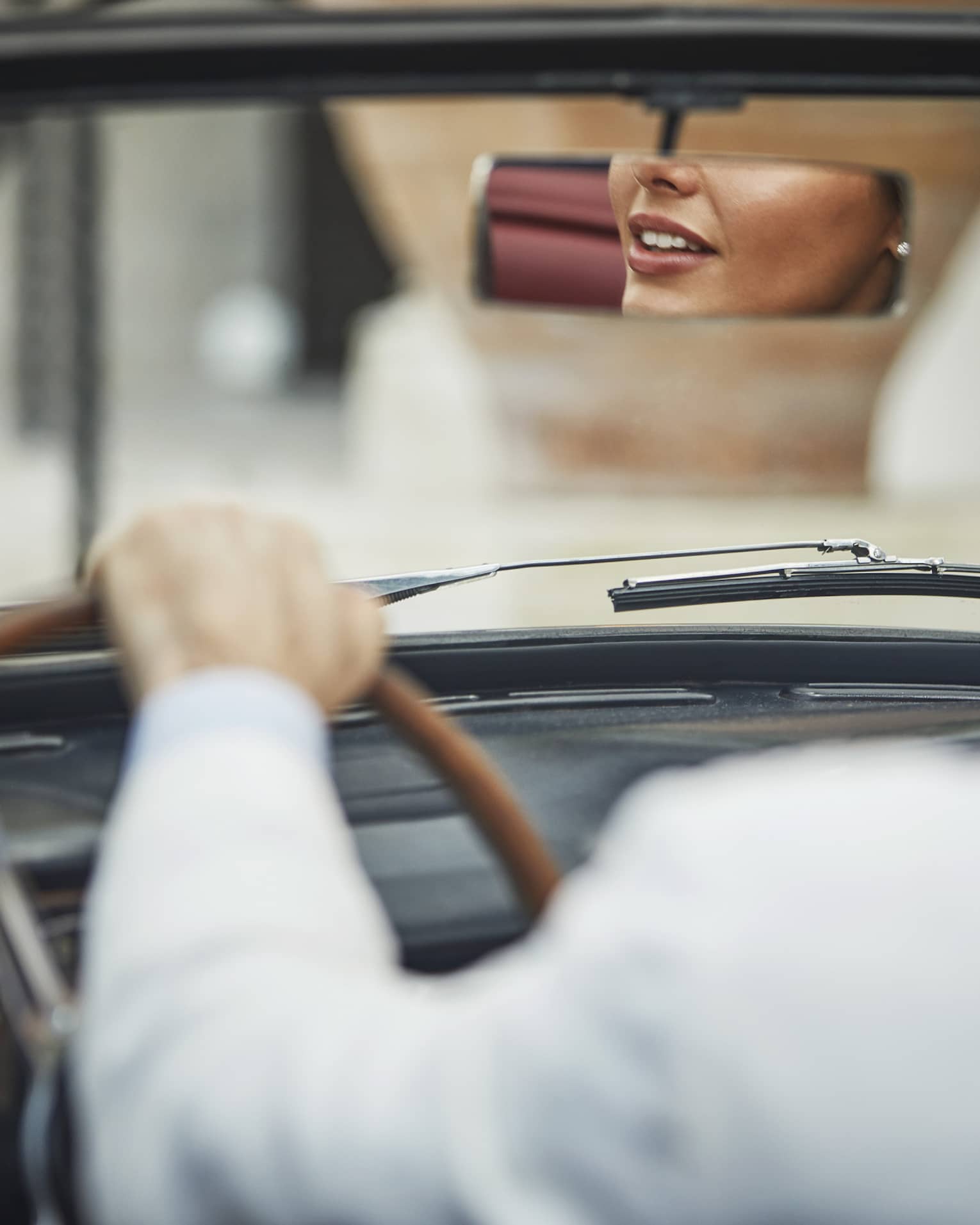 Person driving a convertible car with the reflection of another person in the rear-view mirror.