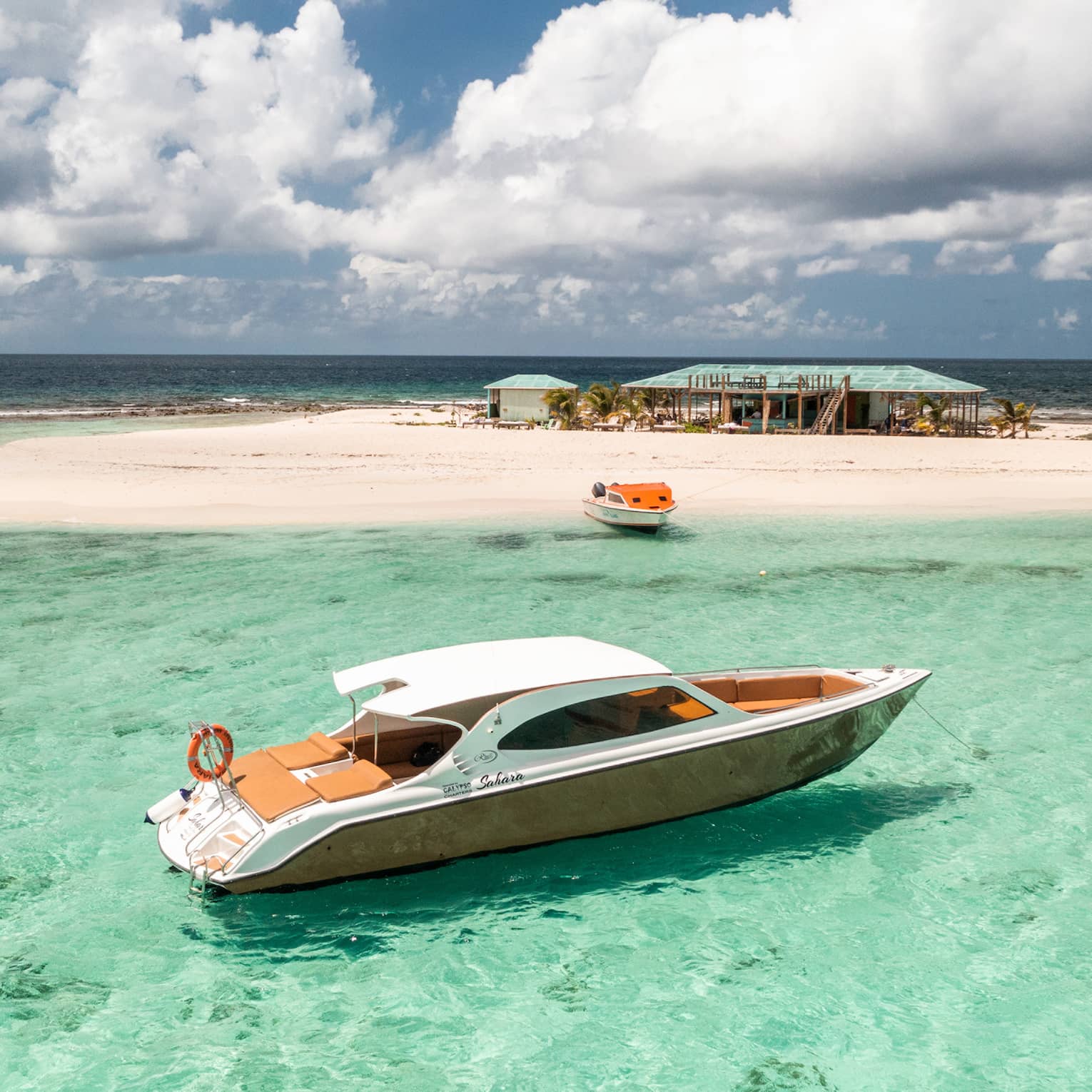 Luxury speedboat floating in clear turquoise water near a sandy island with a beach hut.