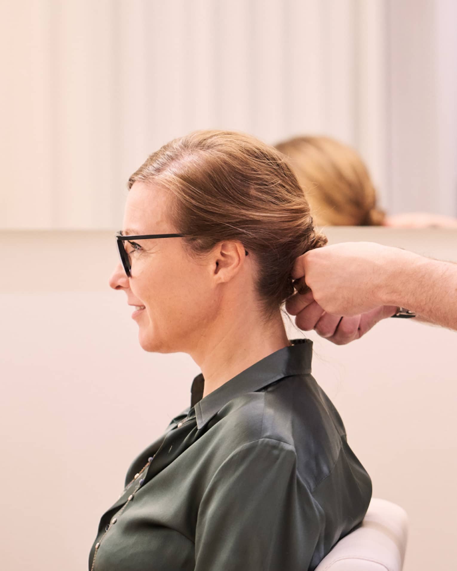 Woman sits in salon chair as hair stylist with long beard holds her hair