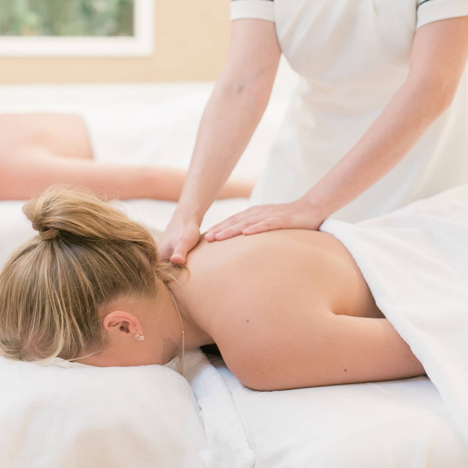 Couple laying on massage tables, spa staff massages woman's shoulders 