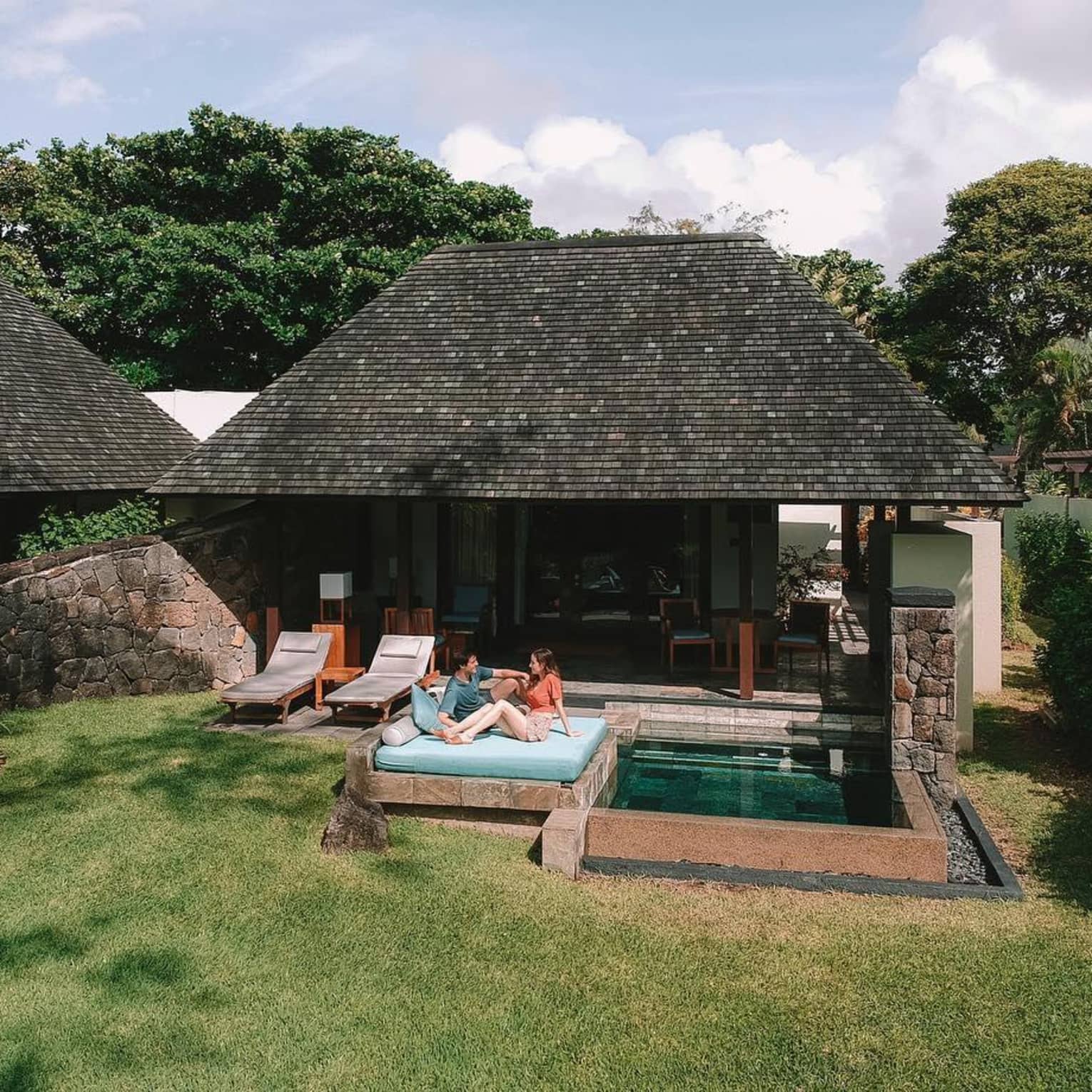 A couple relaxing on a daybed next to a private pool in front of a villa