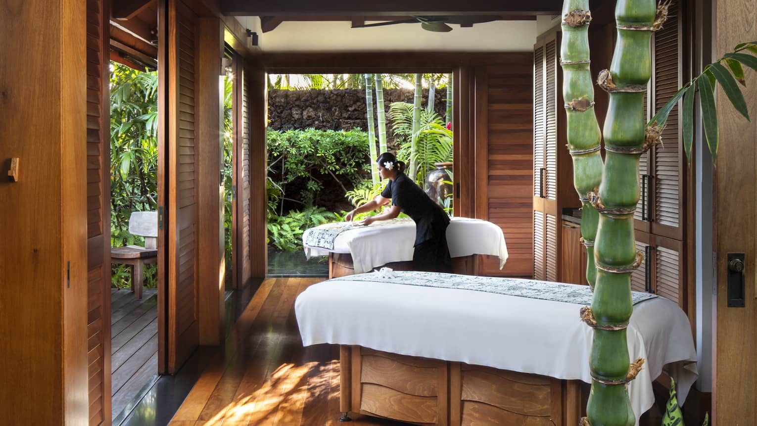 Spa staff spreads sheet on couples massage beds on open-air pavilion 