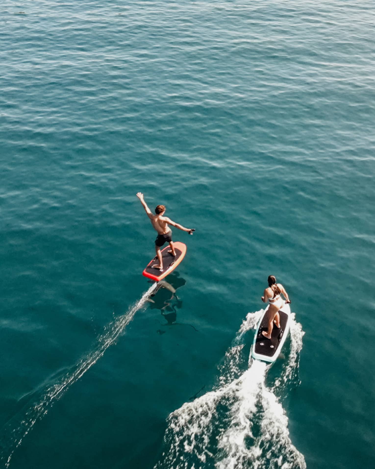 Aerial view of two people riding e0foil surfboards on blue-green water