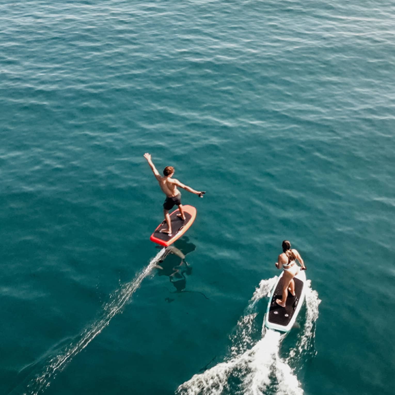 Aerial view of two people riding e0foil surfboards on blue-green water