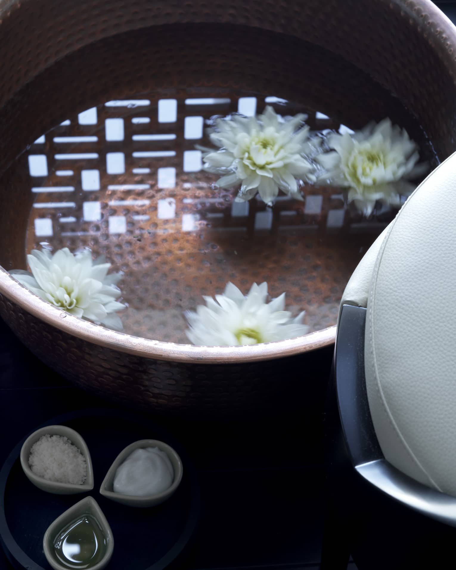 Close-up of copper bowl with water, floating white flowers, small dishes with spa salts, oil and lemons